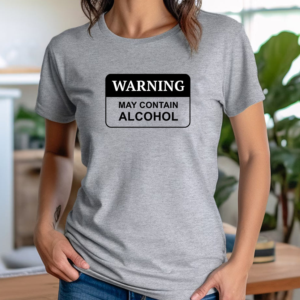 Casual woman standing in a bright modern room wearing the heather grey tee with WARNING may contain alcohol printed design