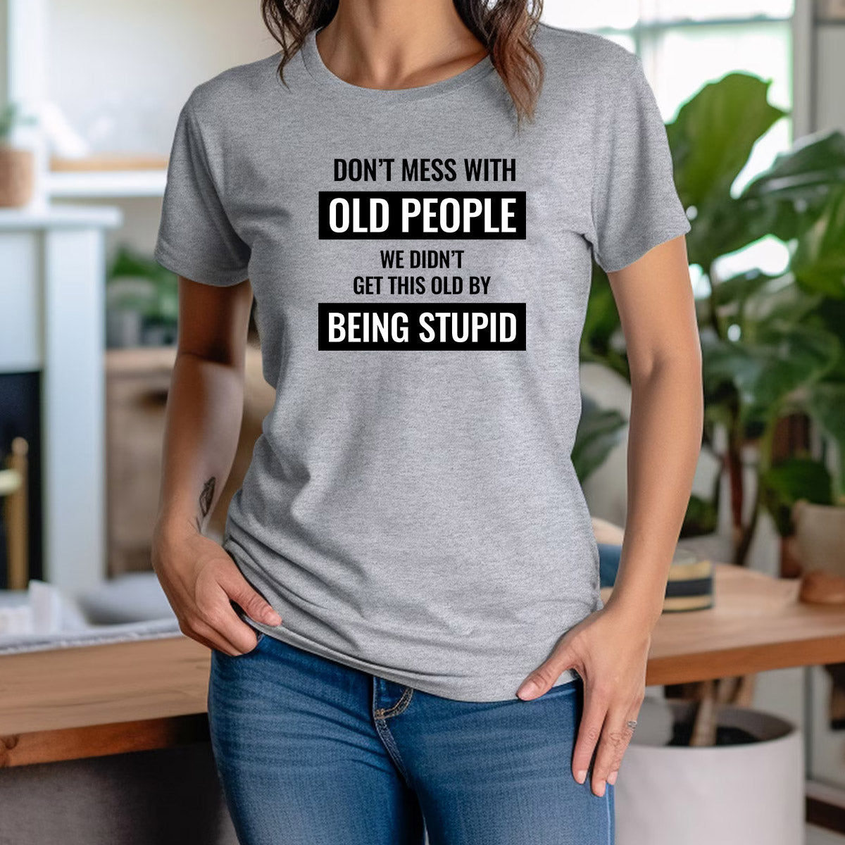 Woman wearing grey graphic t-shirt with text "Don’t mess with old people, we didn’t get this old by being stupid."