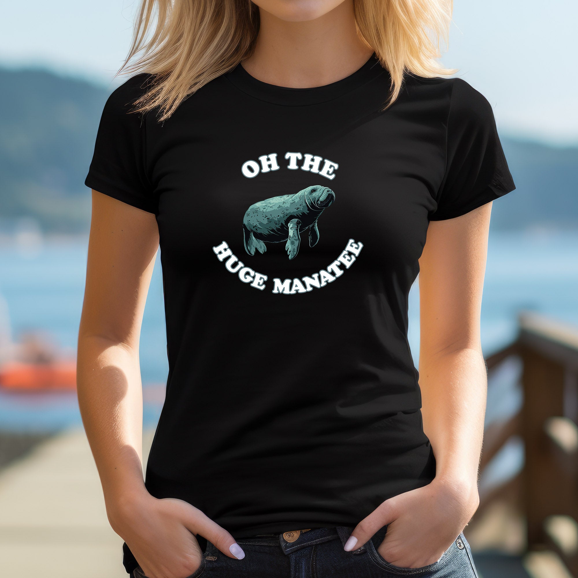 Woman outdoors wearing black t-shirt with cartoon manatee and funny phrase “Oh the Huge Manatee.”
