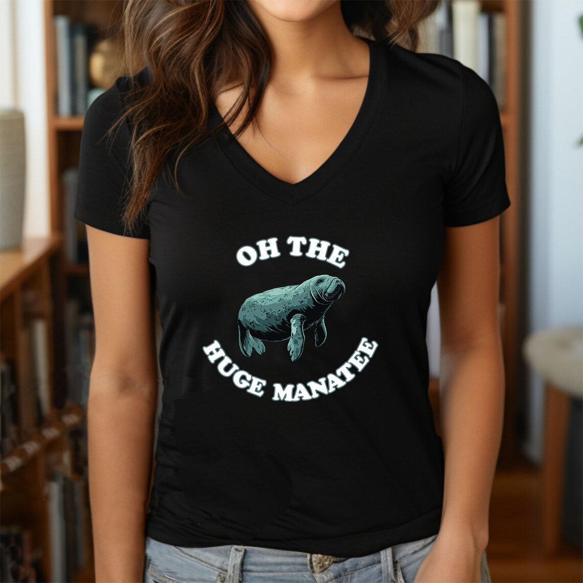 Woman in black v-neck shirt featuring teal manatee illustration with “Oh the Huge Manatee” slogan.