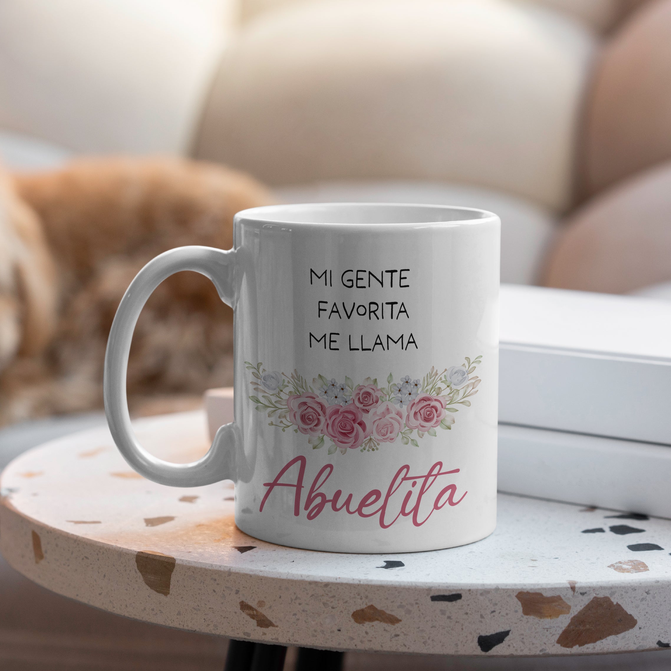 Lifestyle photo of mug with Spanish text Mi gente favorita me llama Abuelita and floral design.
