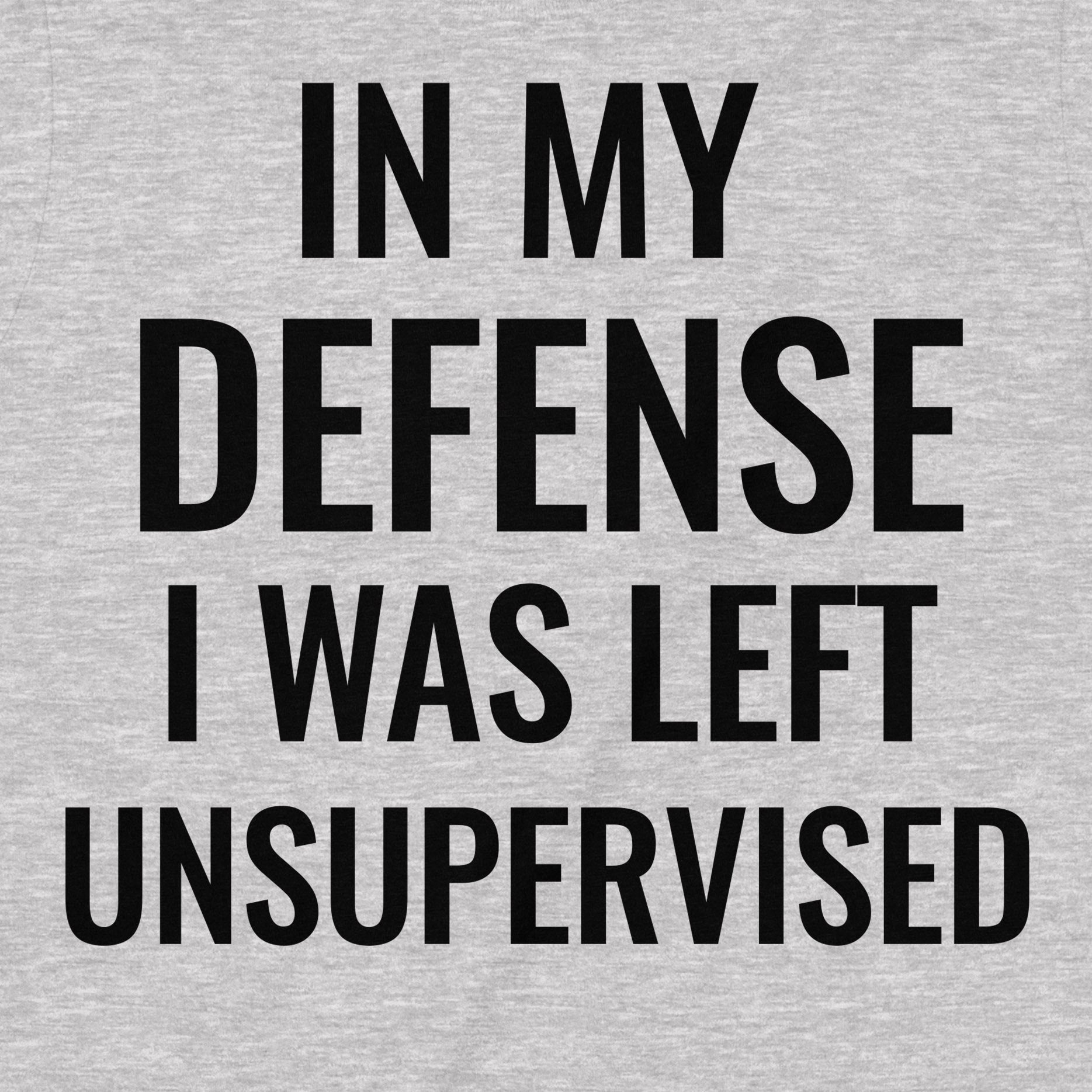 Close-up of black text print reading “In My Defense I Was Left Unsupervised” on a heather grey cotton t-shirt.