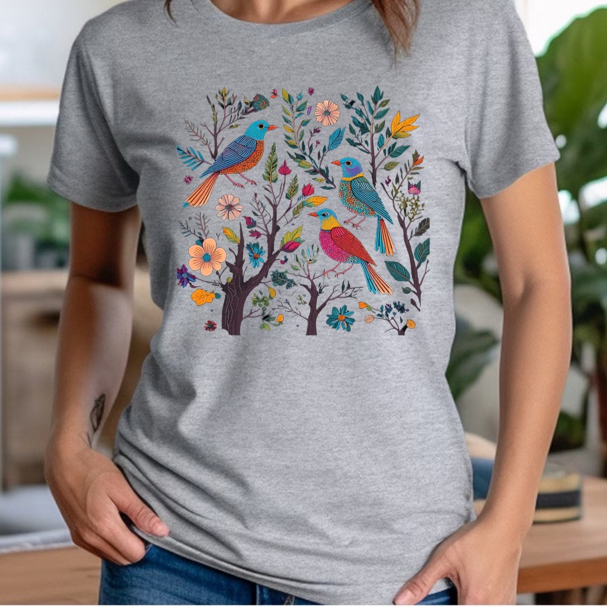 Woman wearing heather gray crewneck t-shirt with colorful songbirds and floral garden illustration