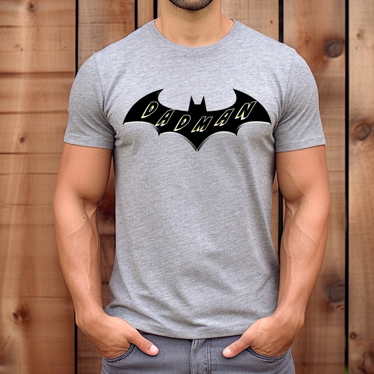 Man wearing grey Dadman superhero t-shirt featuring black bat logo with yellow Dadman text, casual fit.