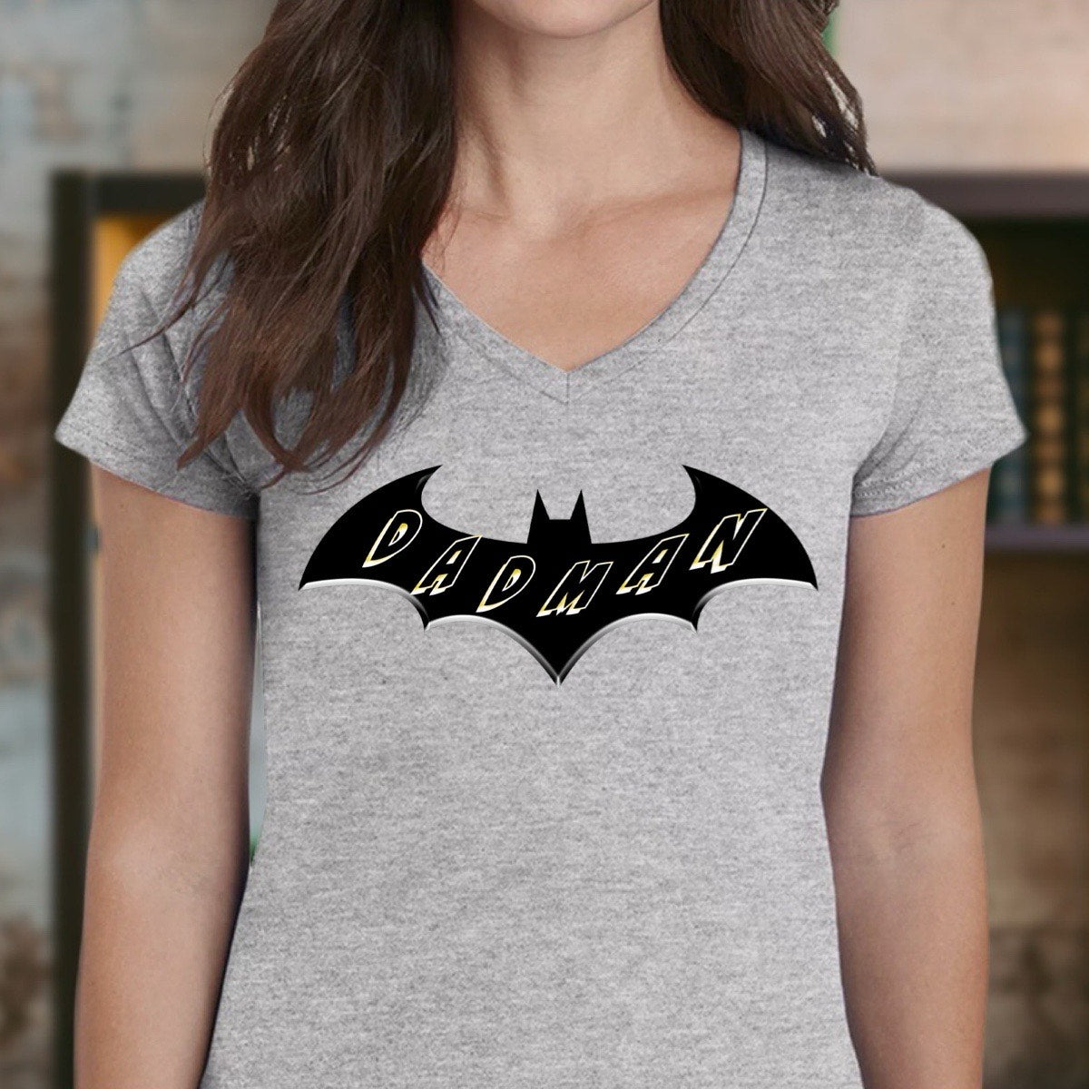 Woman wearing grey v-neck Dadman superhero shirt with black bat logo and bold yellow Dadman lettering.
