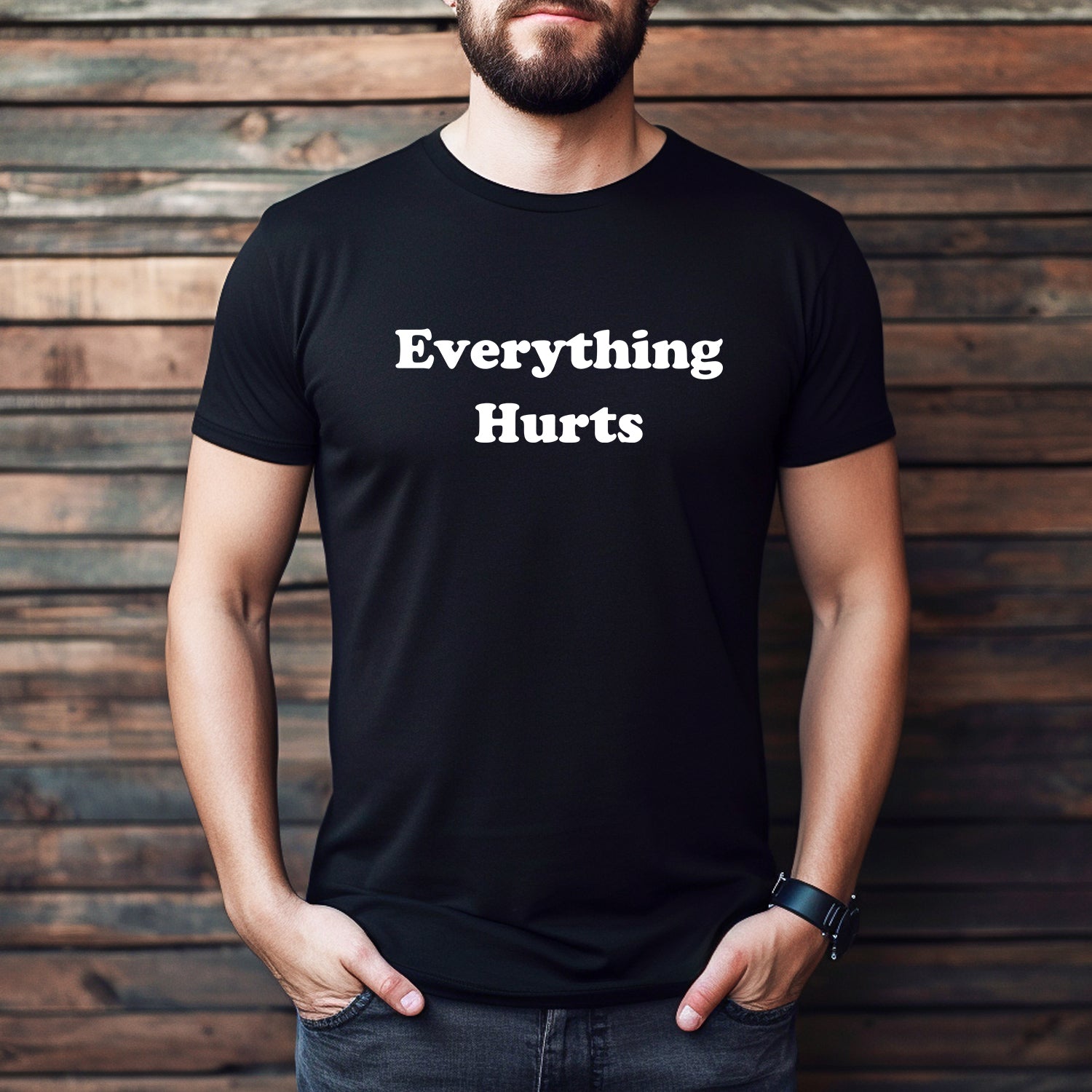 Man wearing black "Everything Hurts" T-shirt standing against wooden background, casual funny gym shirt.