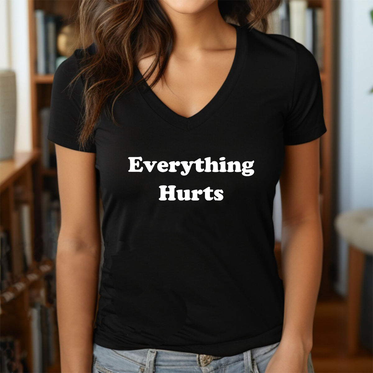 Woman indoors wearing black v-neck T-shirt with white "Everything Hurts" text, humorous women’s tee.