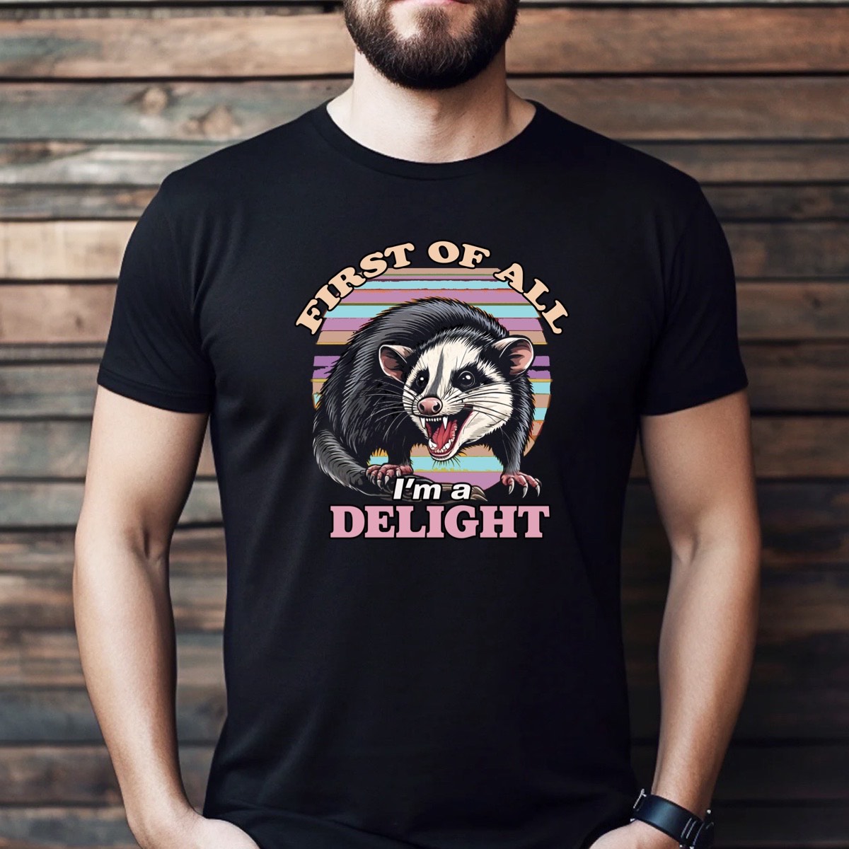 Man wearing black t-shirt featuring opossum graphic with retro stripes and text First of all I’m a delight