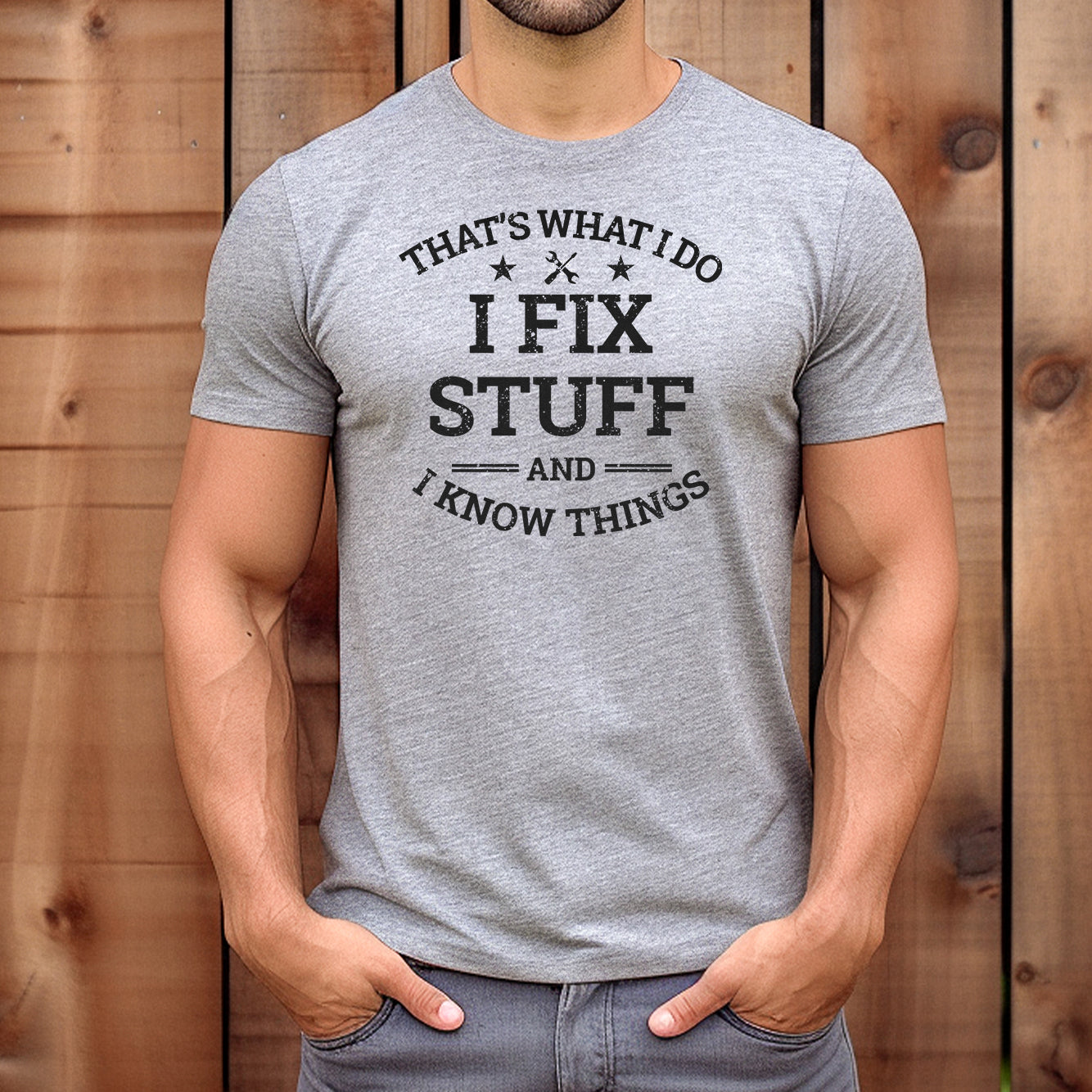 Man wearing grey crew neck t-shirt with I Fix Stuff And I Know Things design standing against wood background