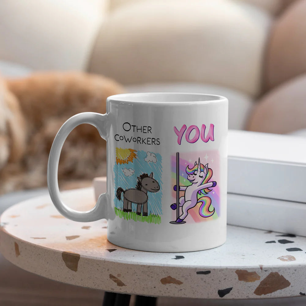 White ceramic coworkers mug with unicorn vs cartoon horse doodle design on table
