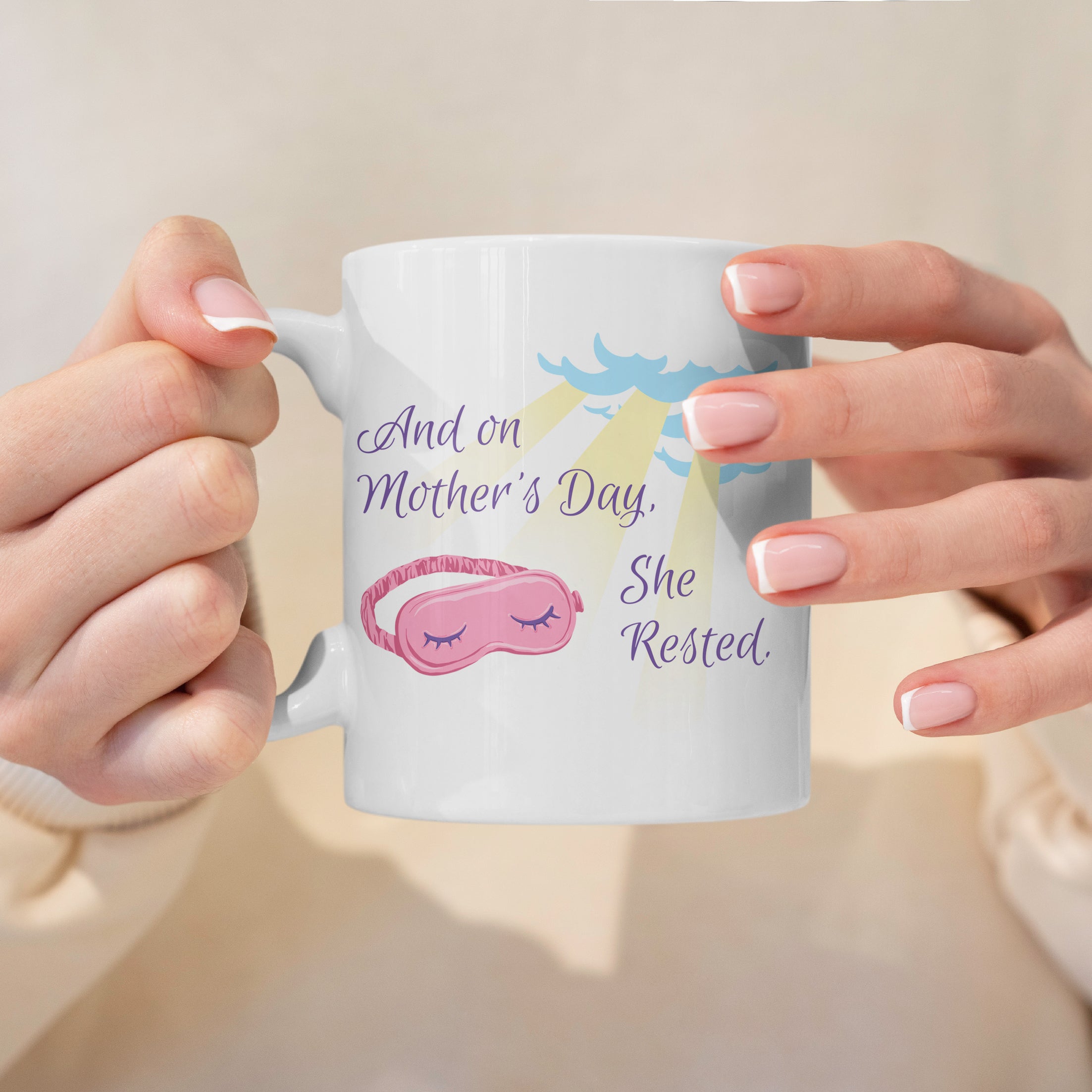 White mug with a humorous Mother's Day message and sleep mask graphic, held by hands against a light background.
