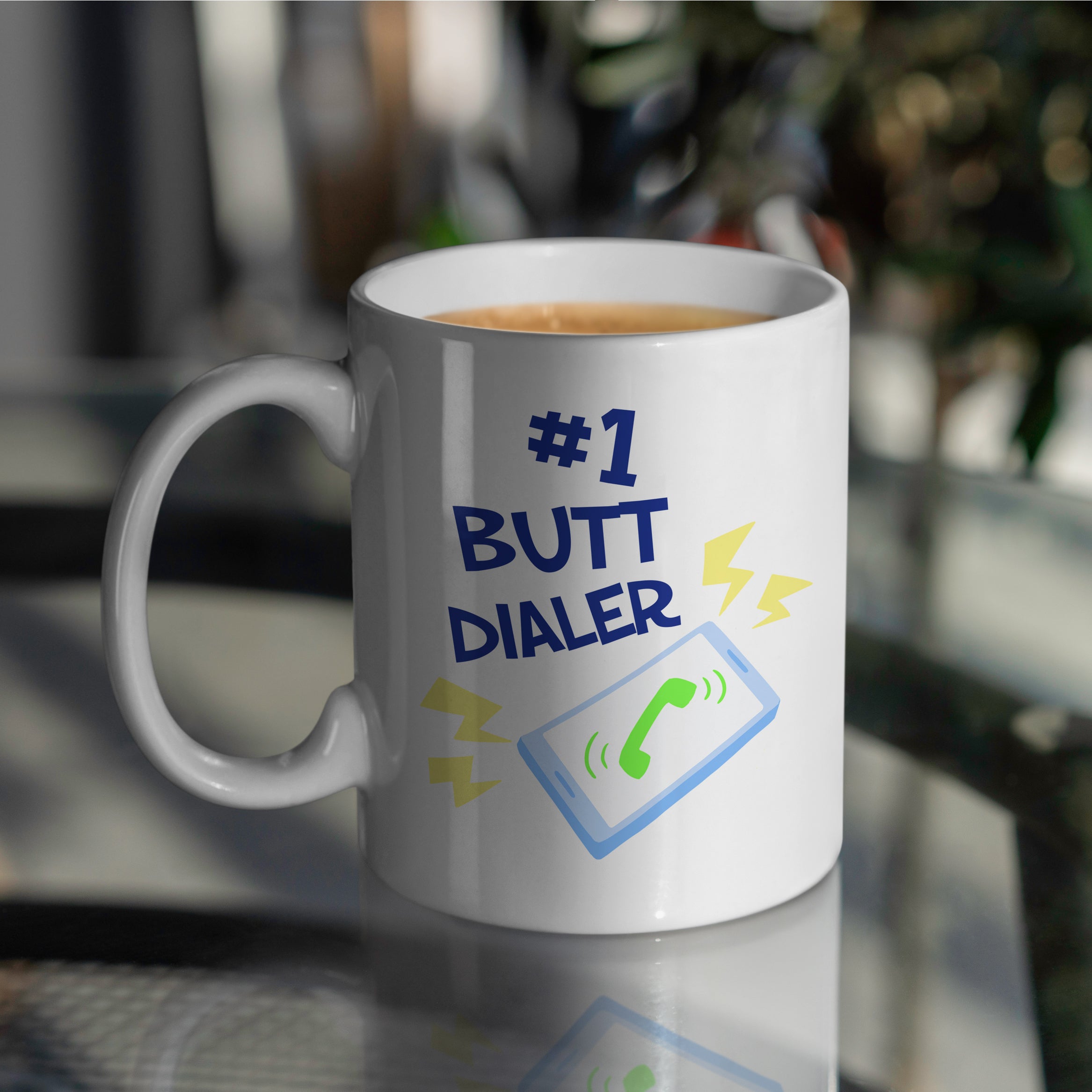 White mug with '#1 Butt Dialer' text and phone icon on glass table 