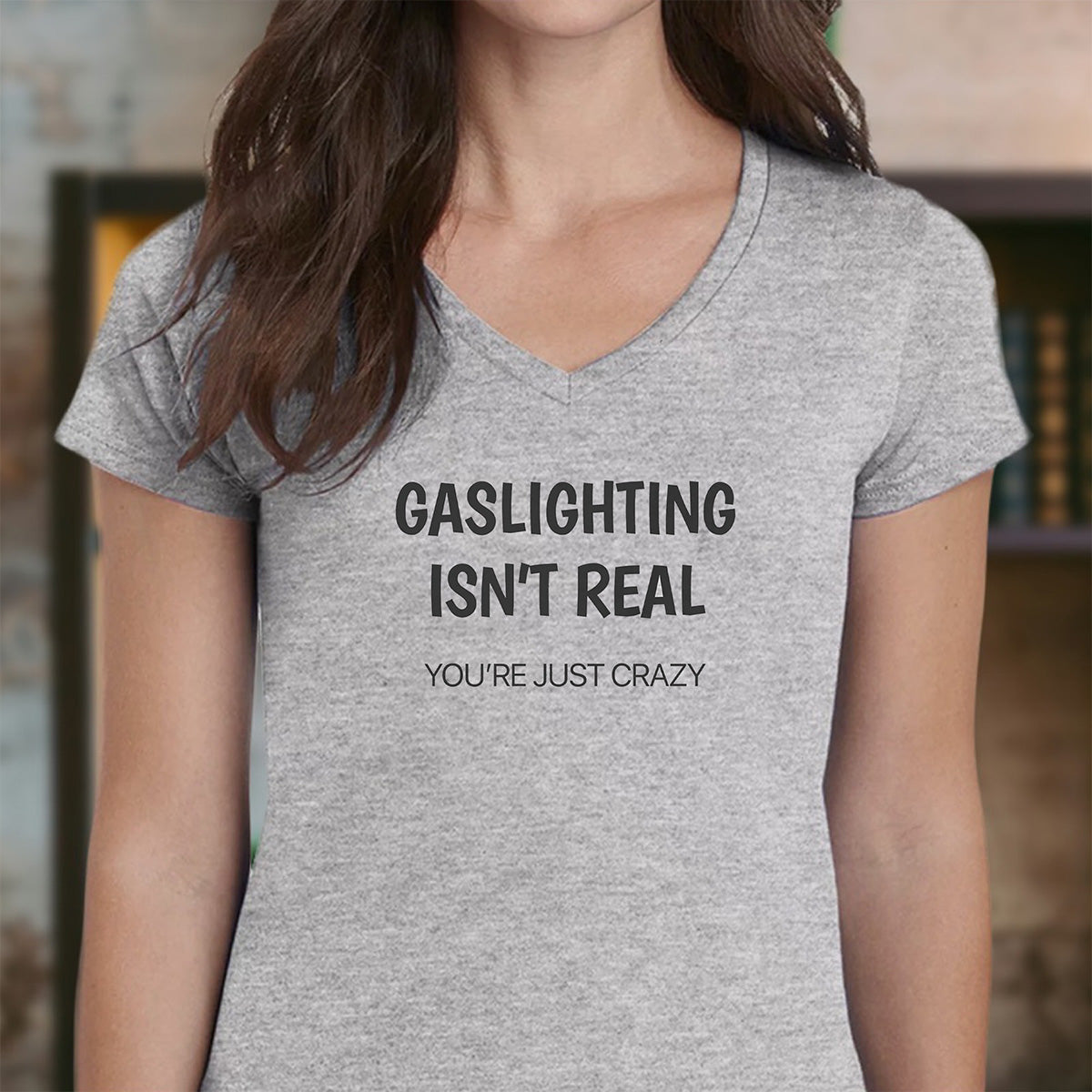Woman wearing gray v-neck shirt with playful statement gaslighting isn’t real you’re just crazy