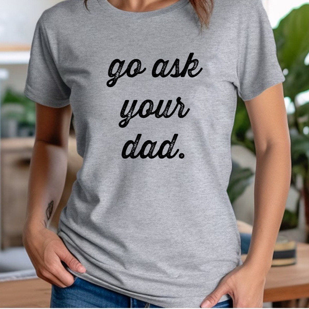 Woman wearing heather gray crewneck tee with go ask your dad script text, relaxed indoor lifestyle