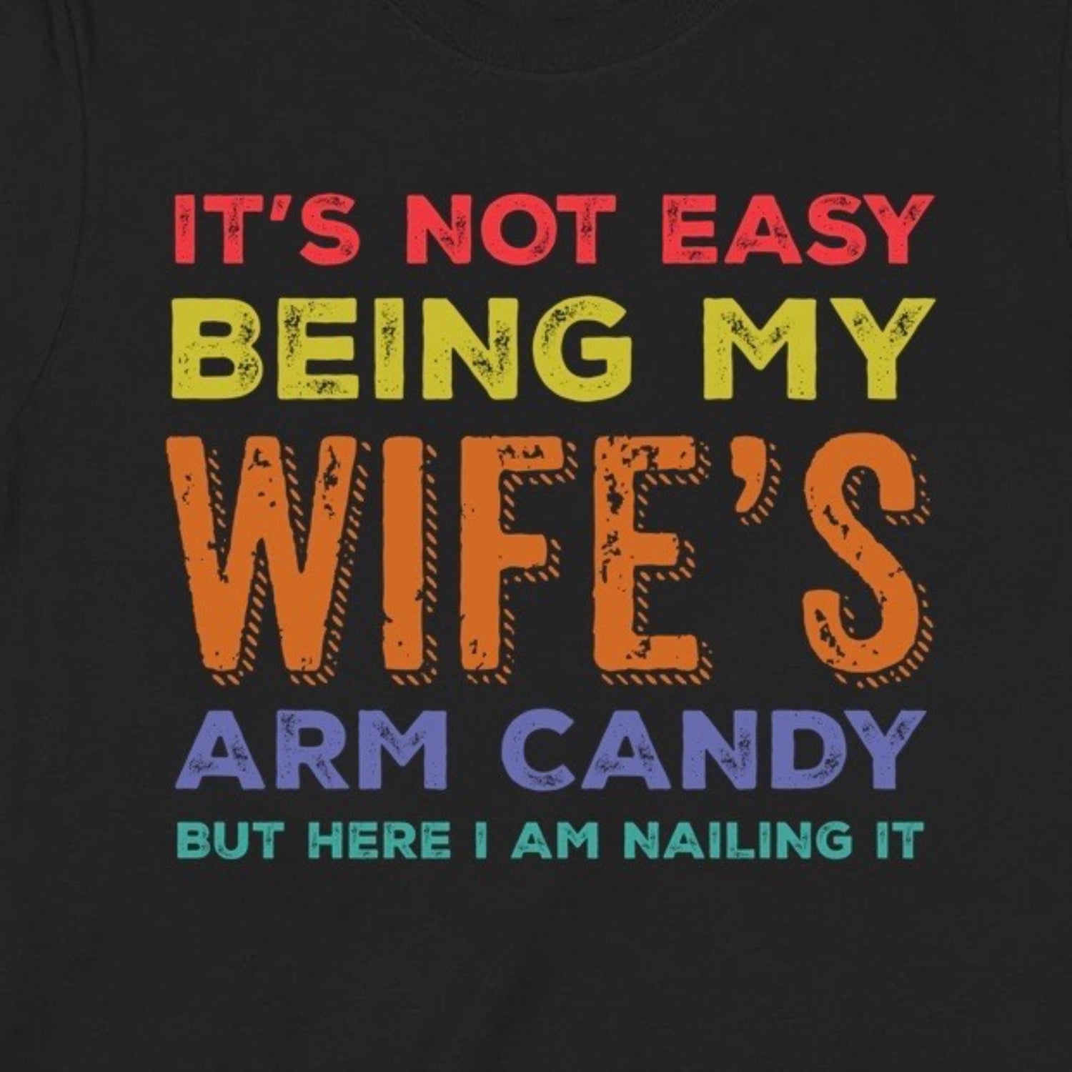 Closeup of colorful graphic text on black shirt reading it's not easy being my wife's arm candy but here I am nailing it