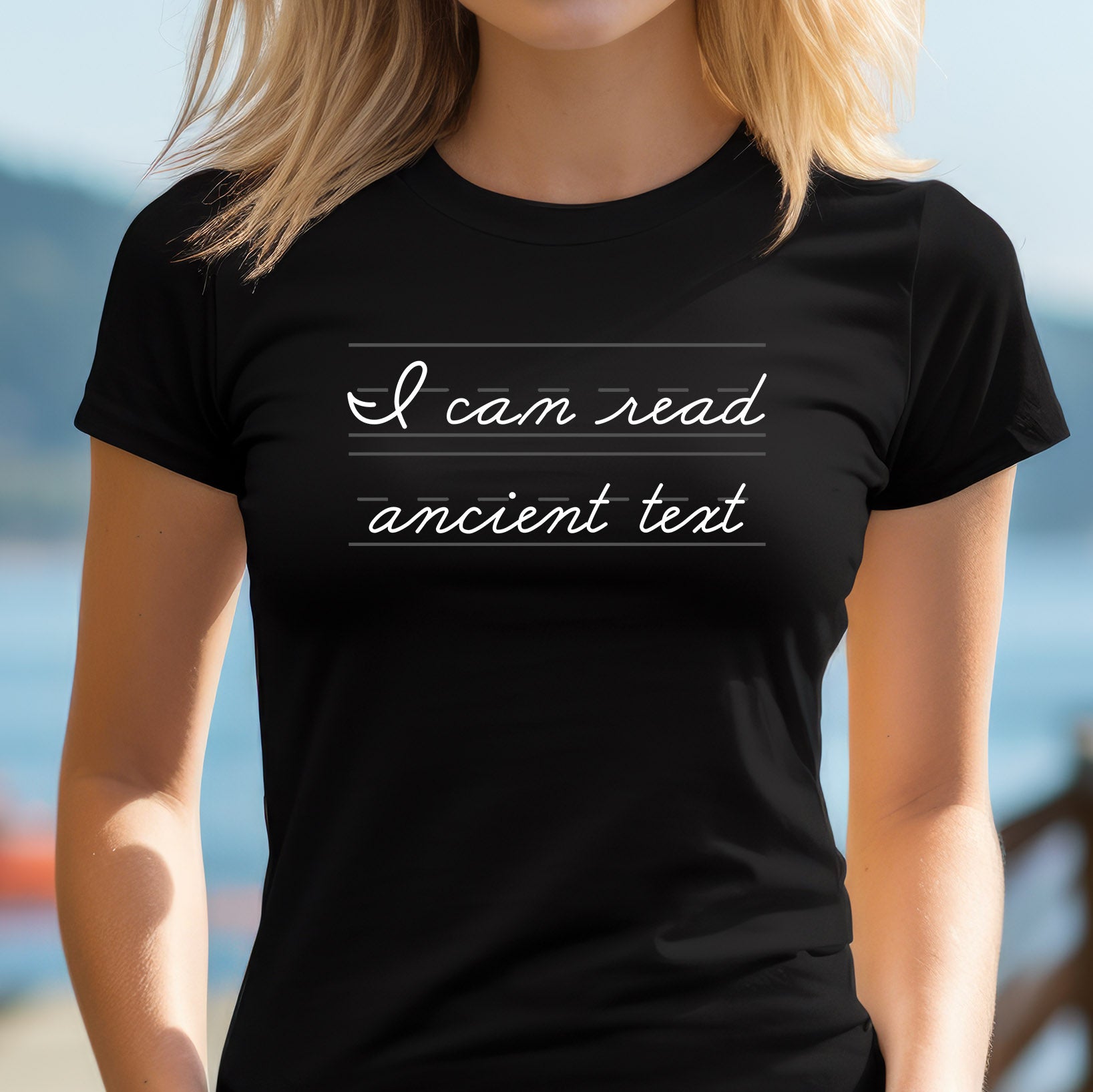 Woman outdoors wearing black t-shirt that says “I can read ancient text” in white cursive handwriting style.