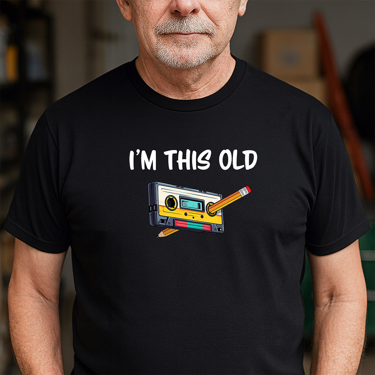 Man wearing black crew neck t-shirt featuring nostalgic cassette tape and pencil with I’m this old text