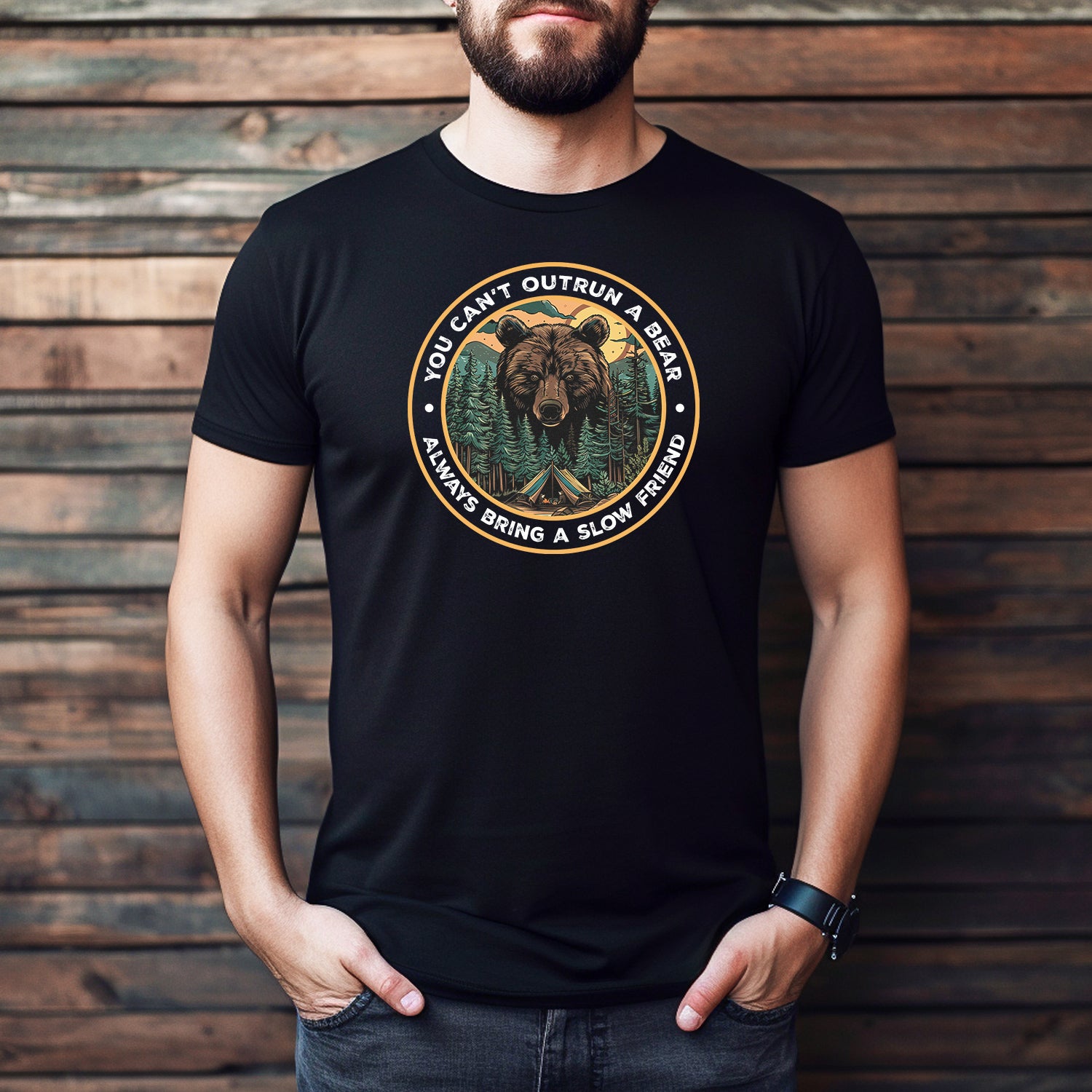 Man wearing black bear camping graphic t-shirt with funny hiking quote, styled with jeans against wood wall