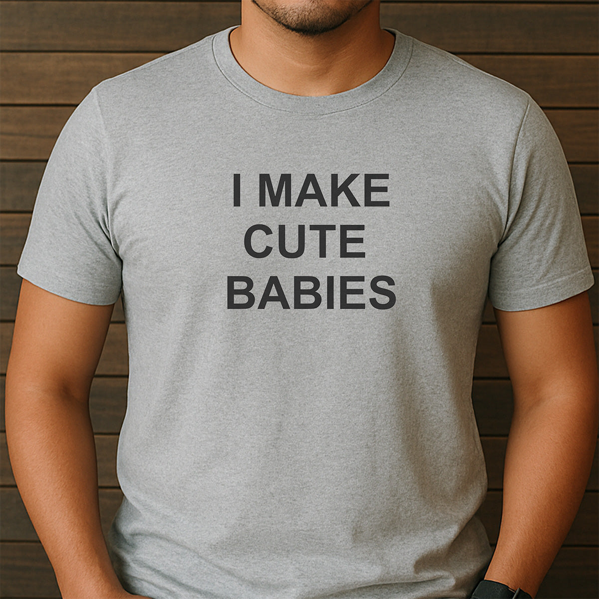 Man wearing heather gray I MAKE CUTE BABIES t-shirt against wood backdrop, casual fit funny dad shirt for Fathers Day