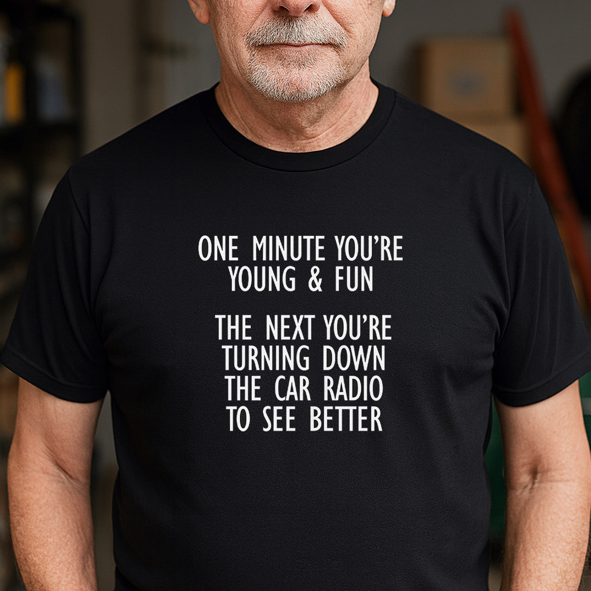 Man wearing black graphic tee with quote about getting older and turning down car radio to see better