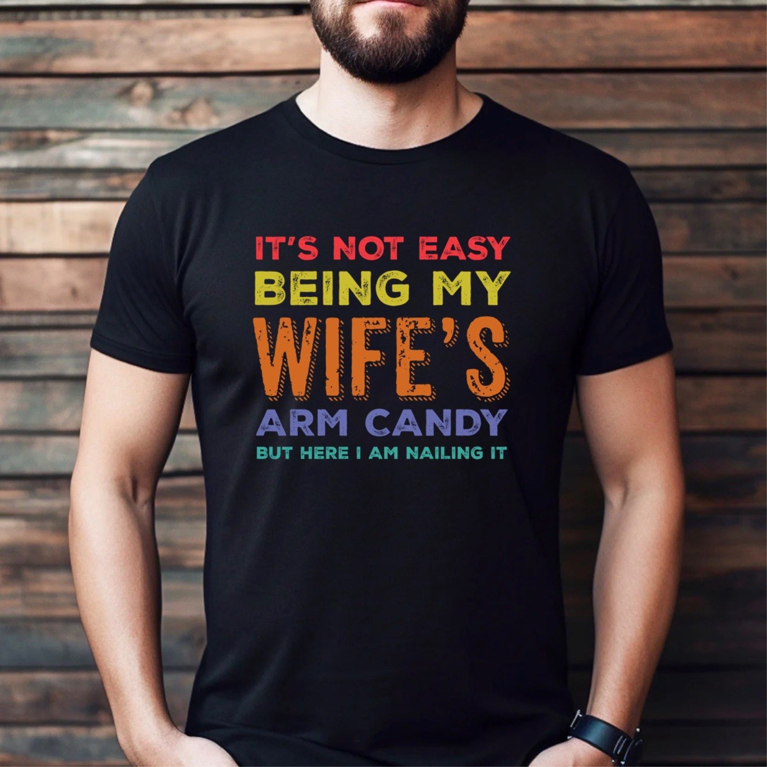 Man wearing black t-shirt with colorful text it's not easy being my wife's arm candy but here I am nailing it