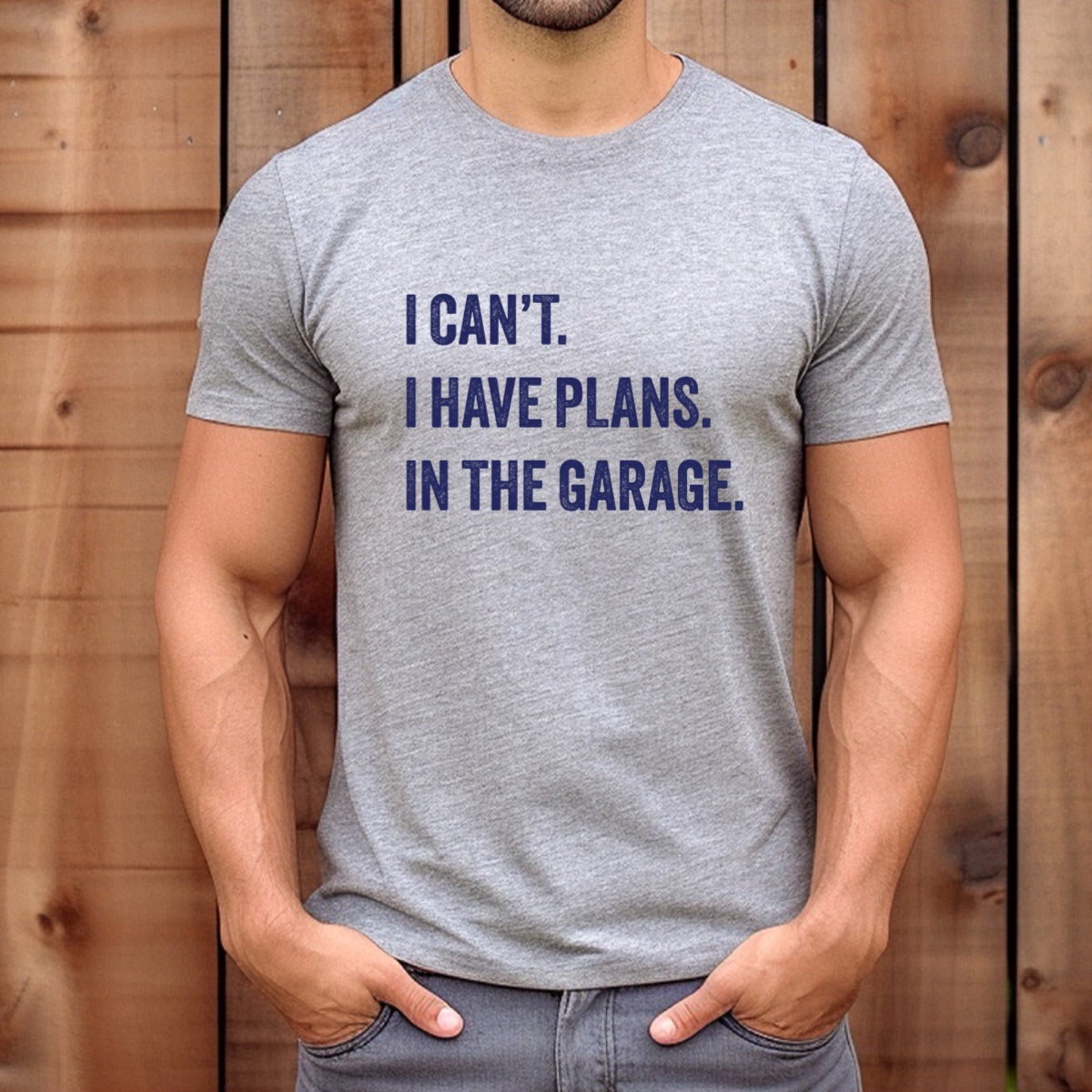 Man wearing fitted grey t-shirt with navy text I can’t I have plans in the garage