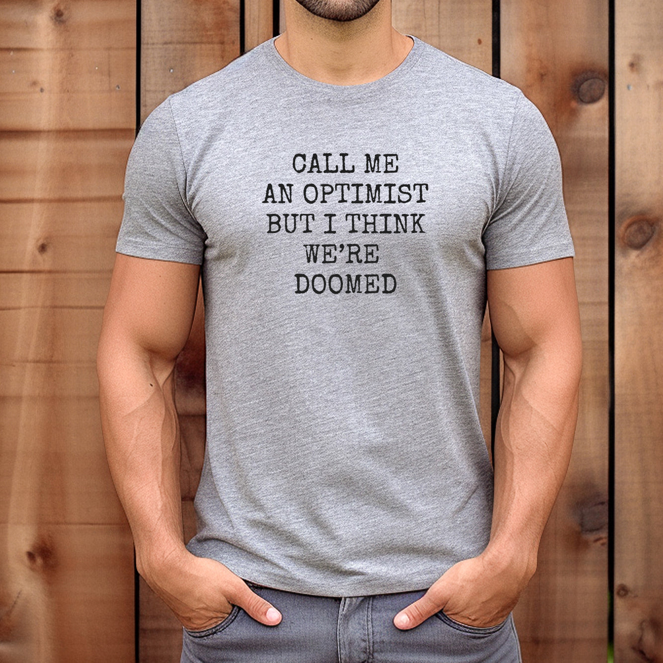 Man standing outdoors wearing grey fitted t-shirt with black text call me an optimist but I think we’re doomed