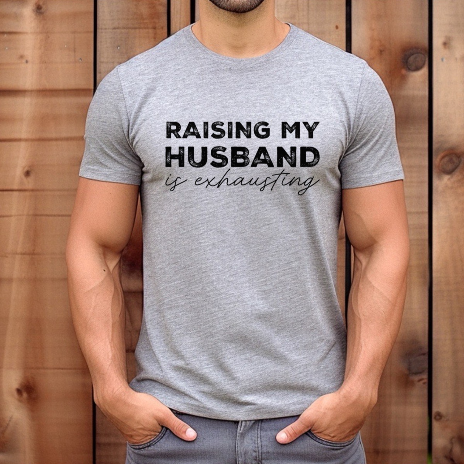 Man wearing grey t-shirt with black text raising my husband is exhausting standing outdoors