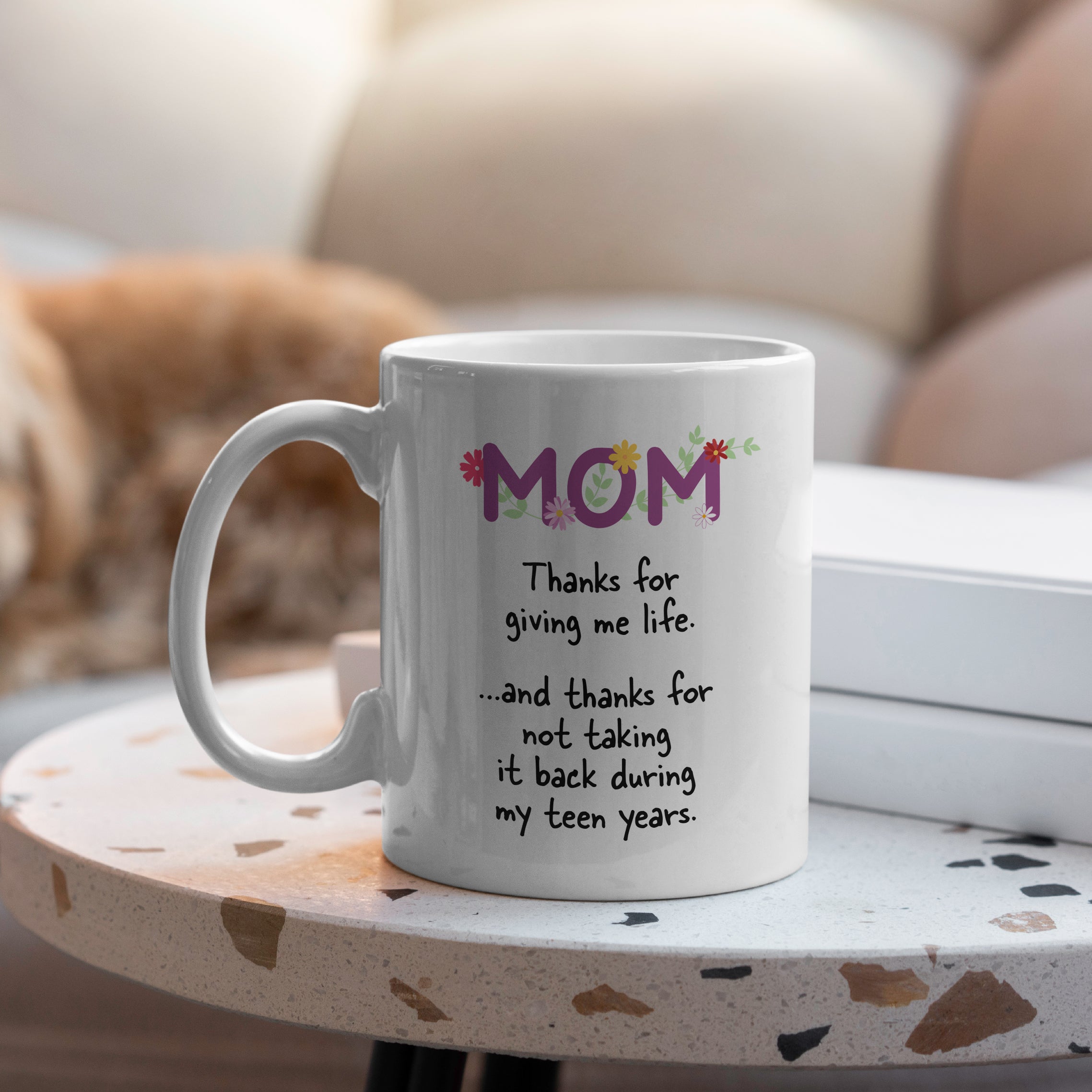 White ceramic mom mug on a table with floral MOM design and humorous teen years quote, perfect gift for moms