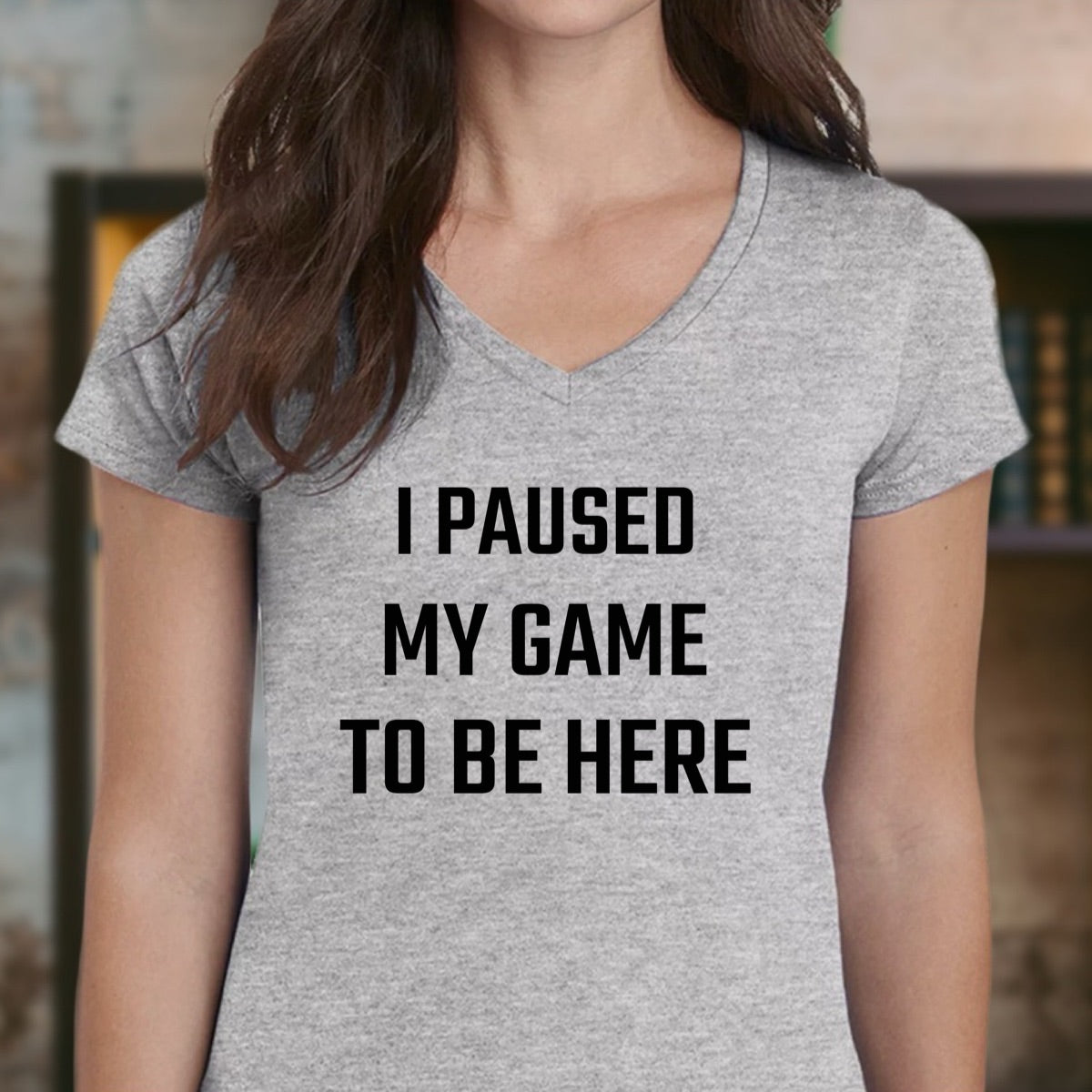 Woman in grey v-neck t-shirt with bold black text I Paused My Game To Be Here, gaming lifestyle clothing