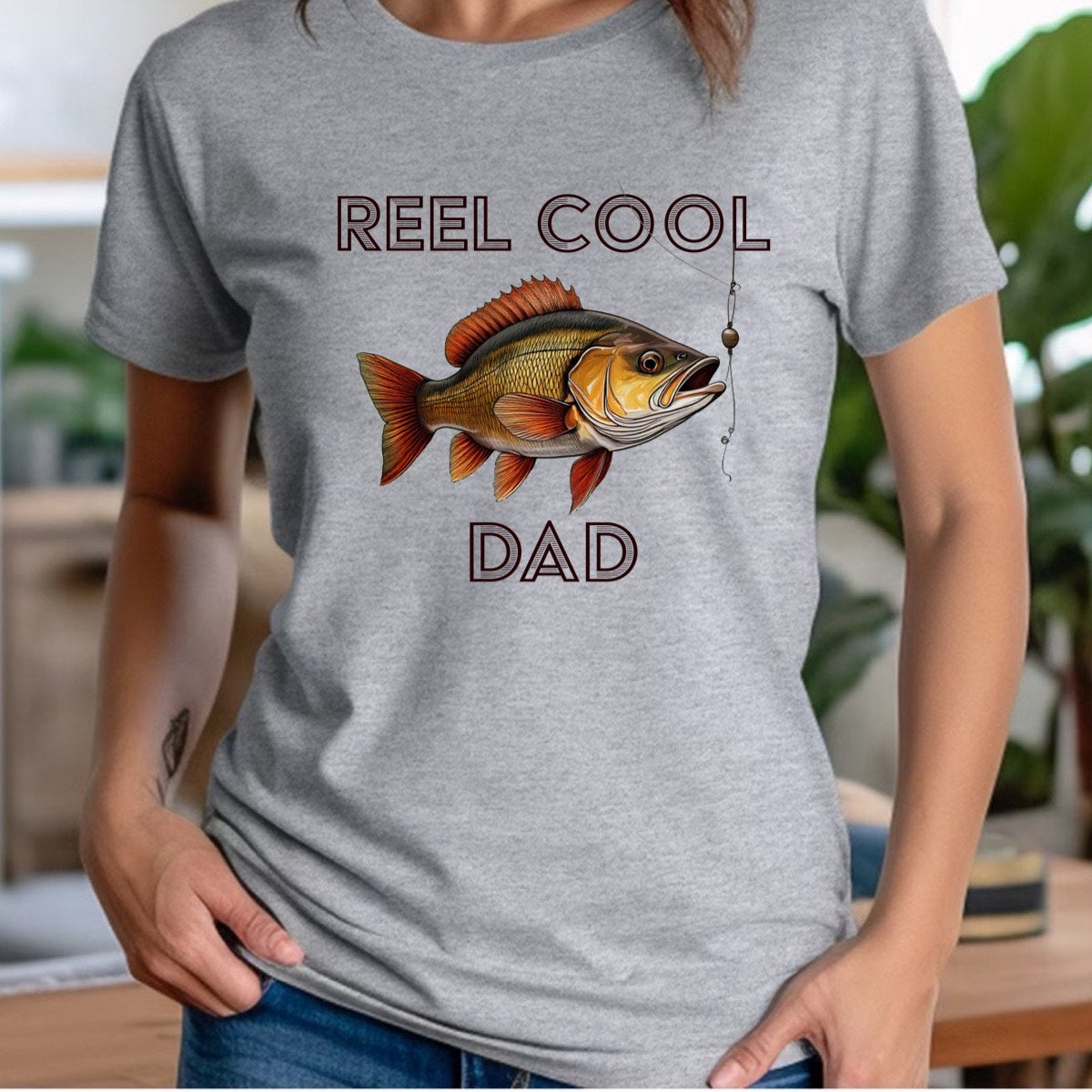 Woman wearing gray crewneck Reel Cool Dad shirt with fish and hook graphic