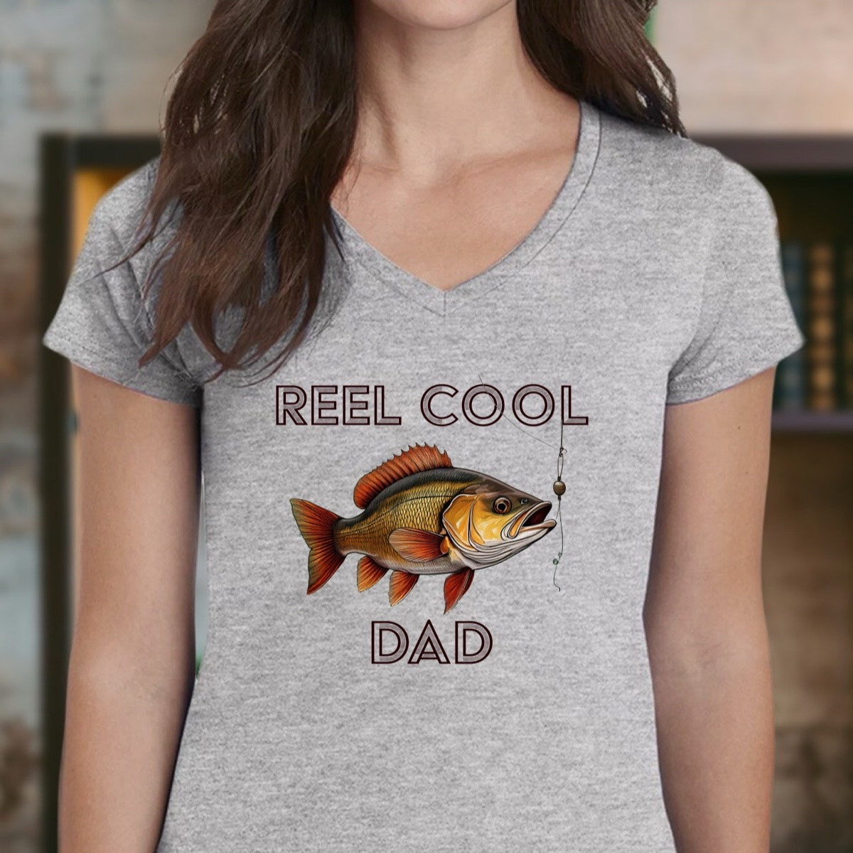 Woman wearing gray v-neck Reel Cool Dad fishing shirt with fish illustration and hook design