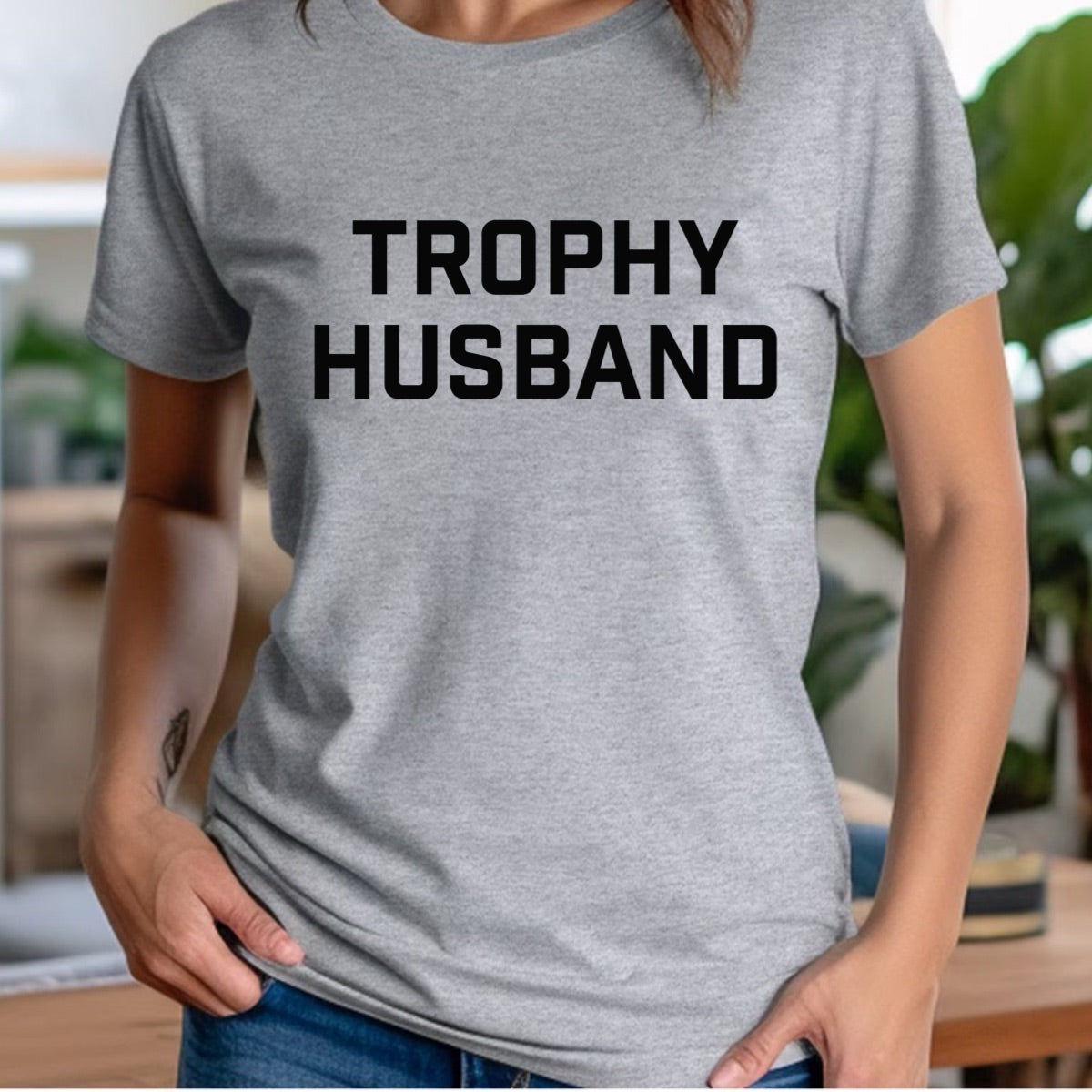 Woman in gray crewneck Trophy Husband t-shirt with bold black text