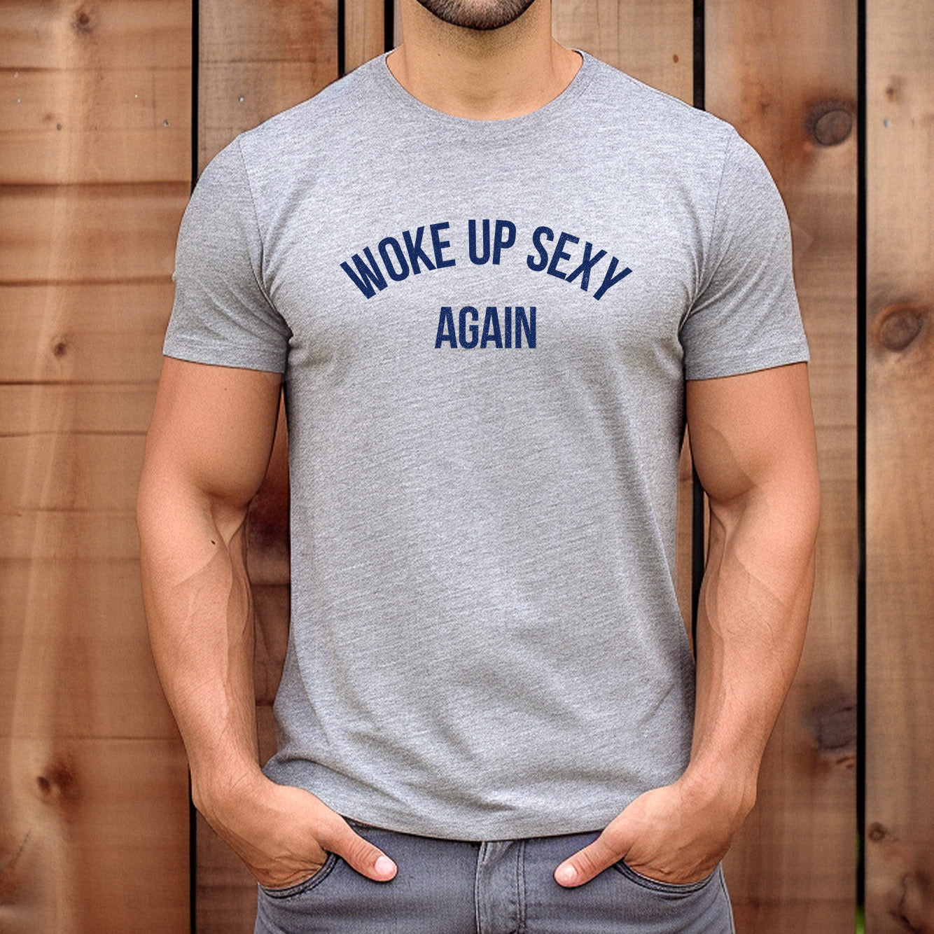 Man wearing fitted grey t-shirt with bold navy print "Woke Up Sexy Again" standing by wooden wall.