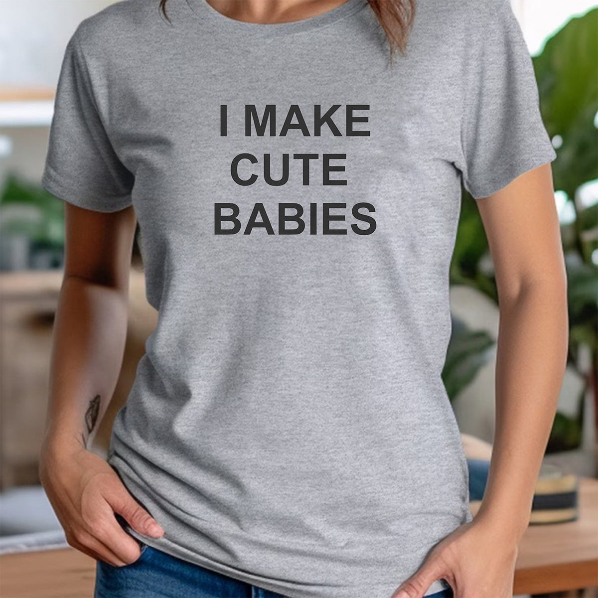 Woman in heather gray crewneck tee with I MAKE CUTE BABIES text, relaxed fit unisex funny parent shirt indoors