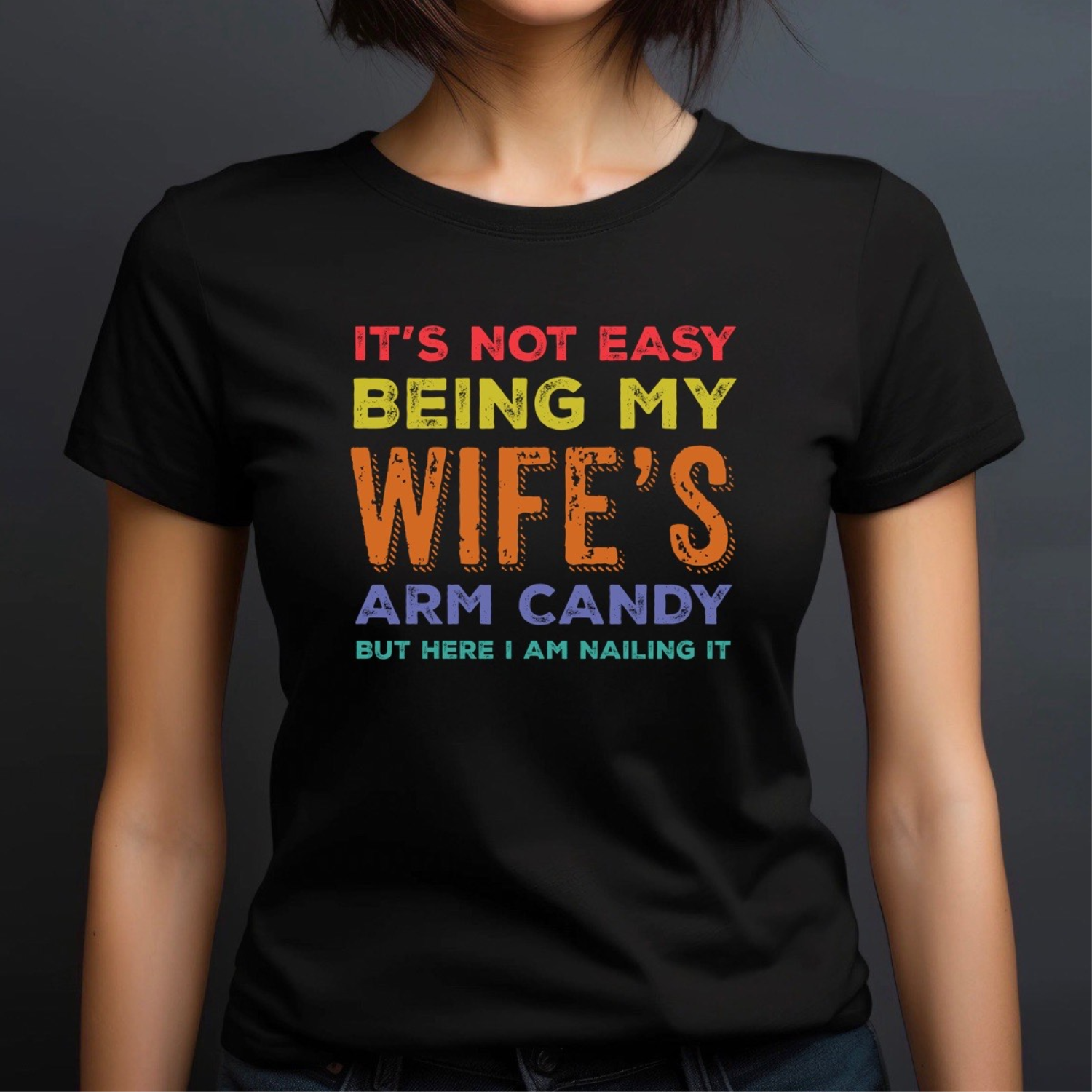 Woman wearing crewneck black t-shirt with colorful text it's not easy being my wife's arm candy but here I am nailing it