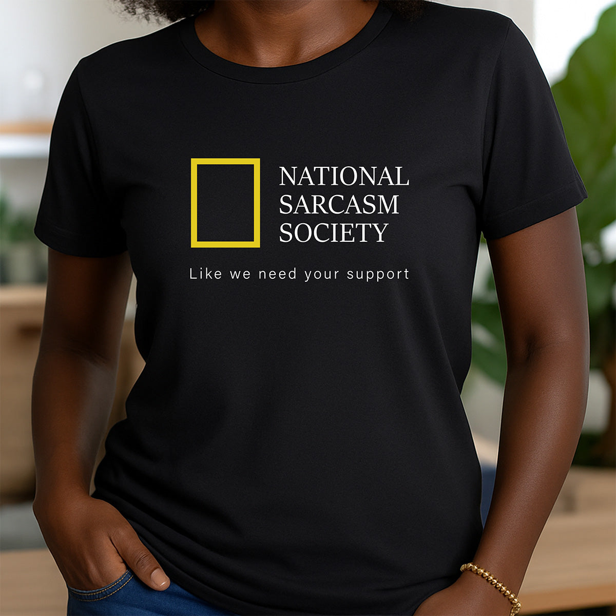 Woman wearing black crewneck t-shirt with National Sarcasm Society graphic and slogan Like we need your support