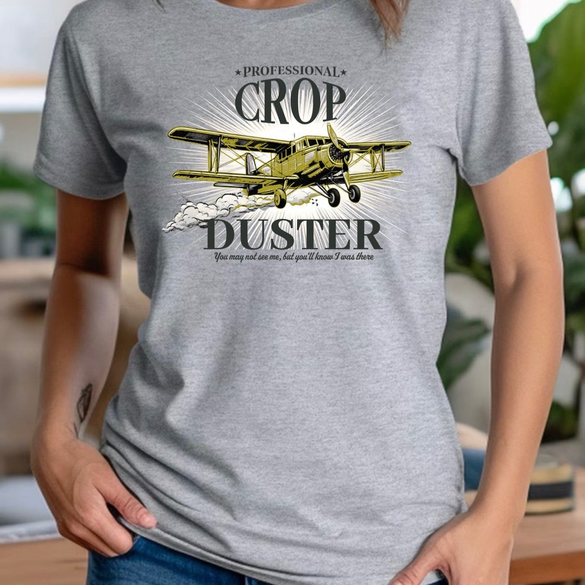 Woman in grey crewneck shirt featuring yellow crop duster airplane and text professional crop duster