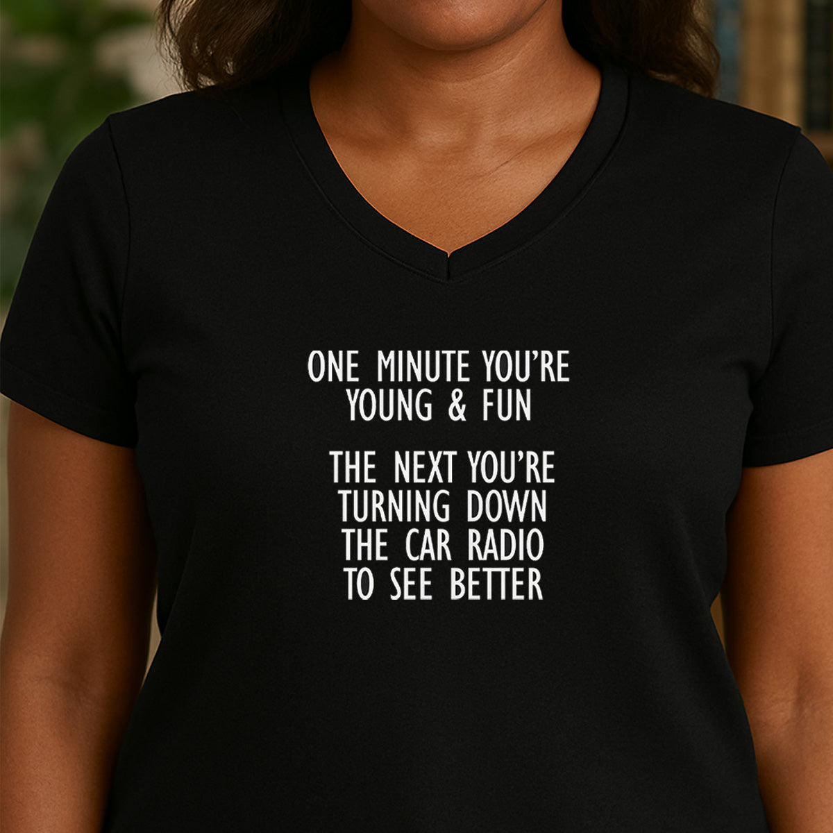 Woman in black v-neck shirt with humorous quote about aging and turning down car radio to see better