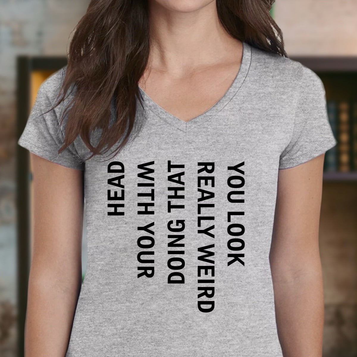 Woman wearing grey v-neck shirt with vertical text design saying you look really weird doing that with your head