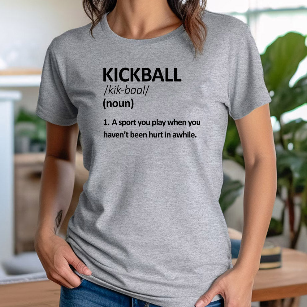 Woman in fitted grey kickball definition t-shirt with witty printed sports quote at home.