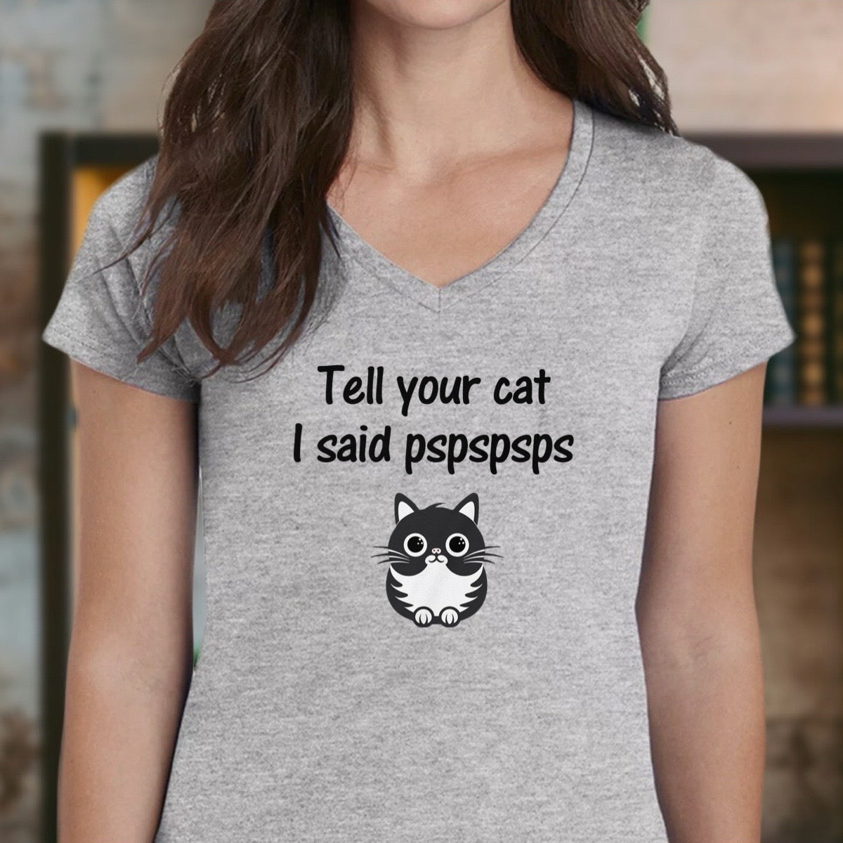 Woman wearing grey v-neck t-shirt with cartoon cat graphic and phrase “Tell your cat I said pspspsps.”