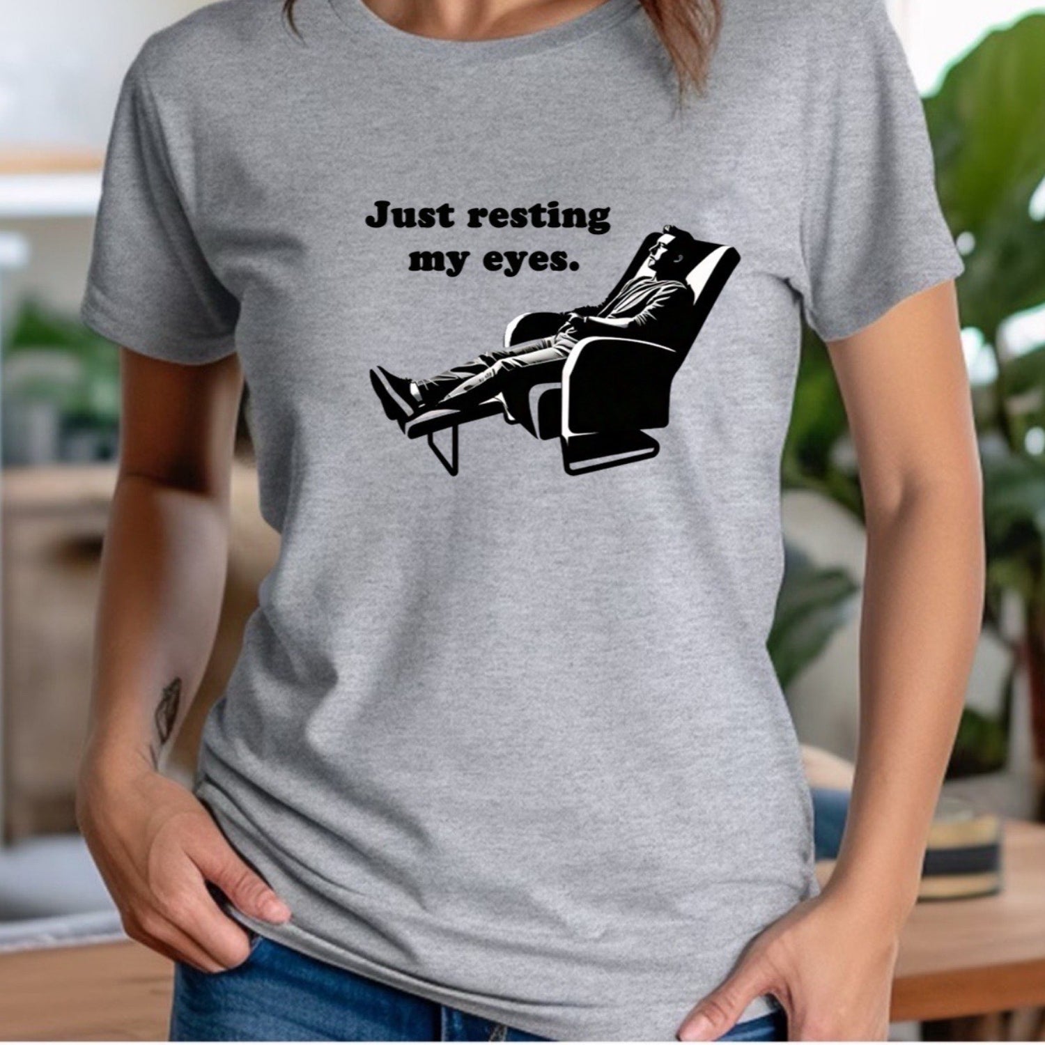Woman in grey crew neck shirt with Just resting my eyes text and chair graphic