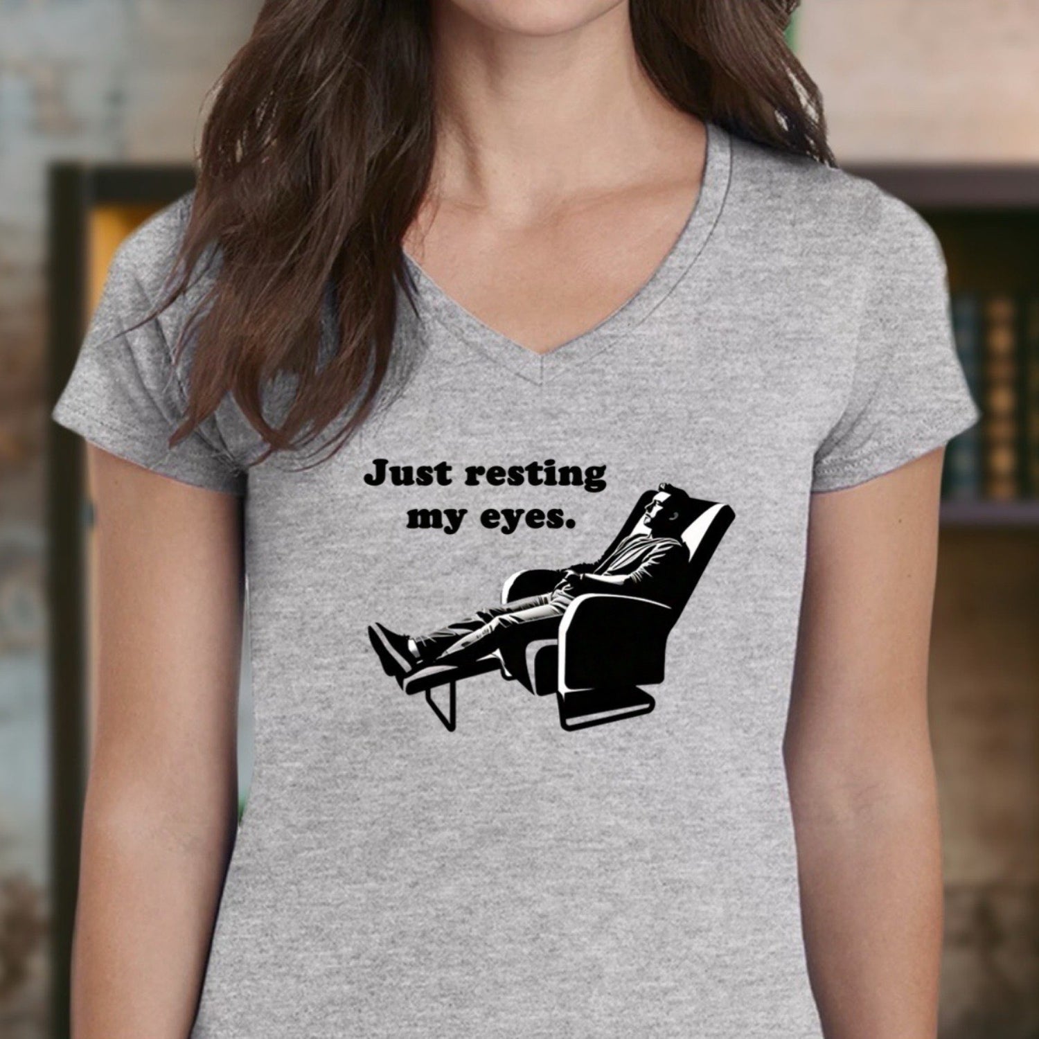 Woman in grey v-neck t-shirt with Just resting my eyes slogan and reclining man graphic