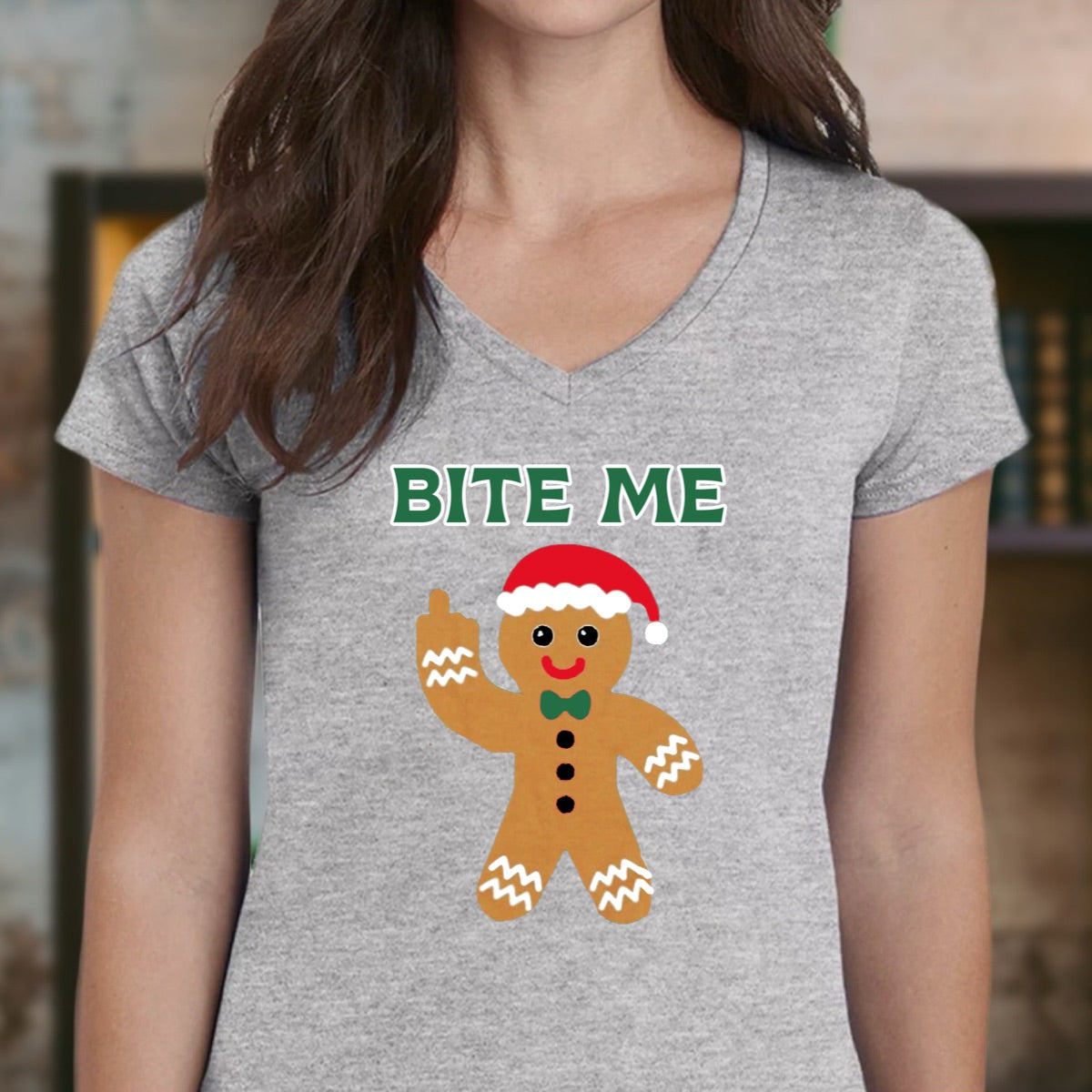 Woman in grey V-neck Christmas shirt with gingerbread Bite Me Santa hat design