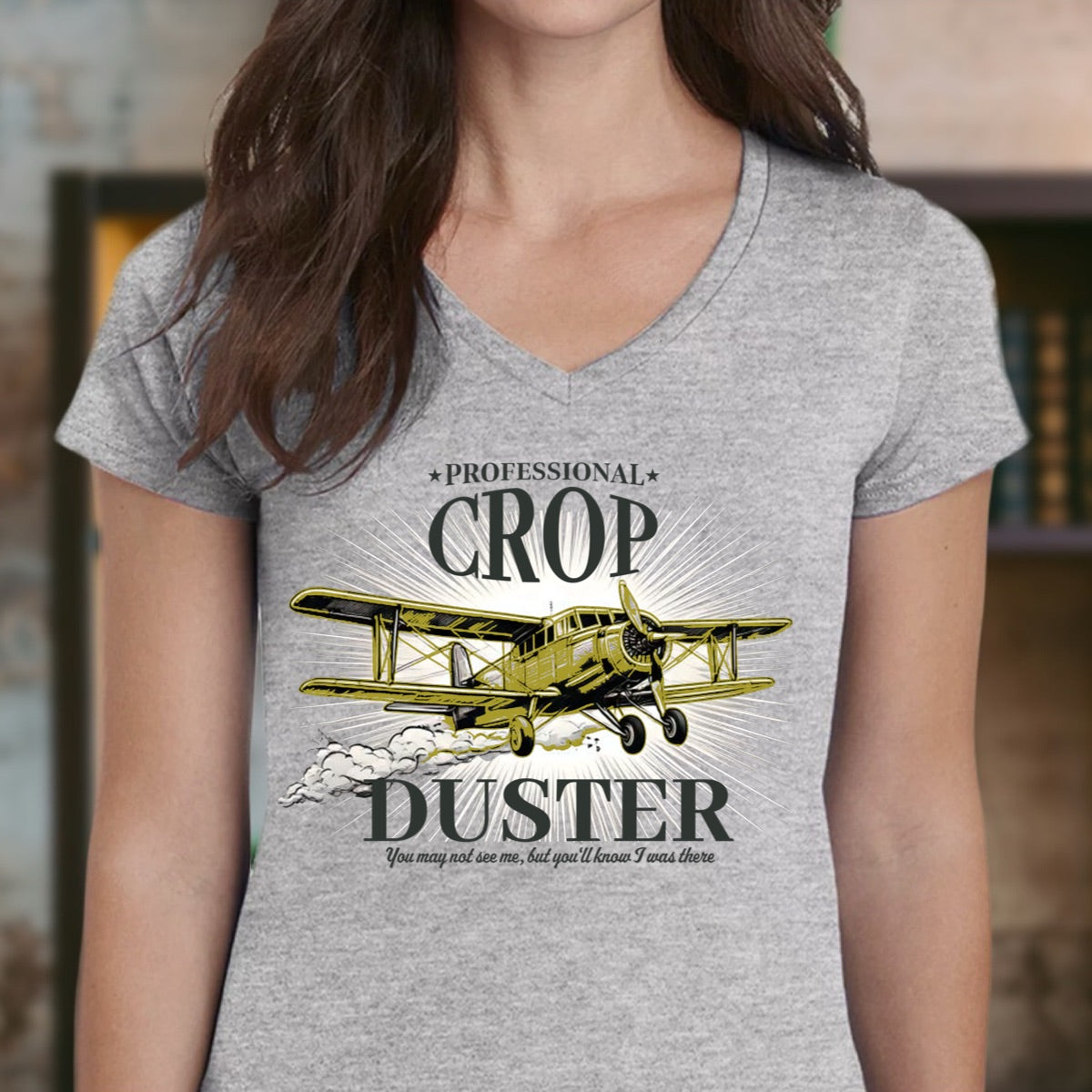 Woman wearing grey v-neck t-shirt with yellow crop duster airplane graphic and professional crop duster slogan