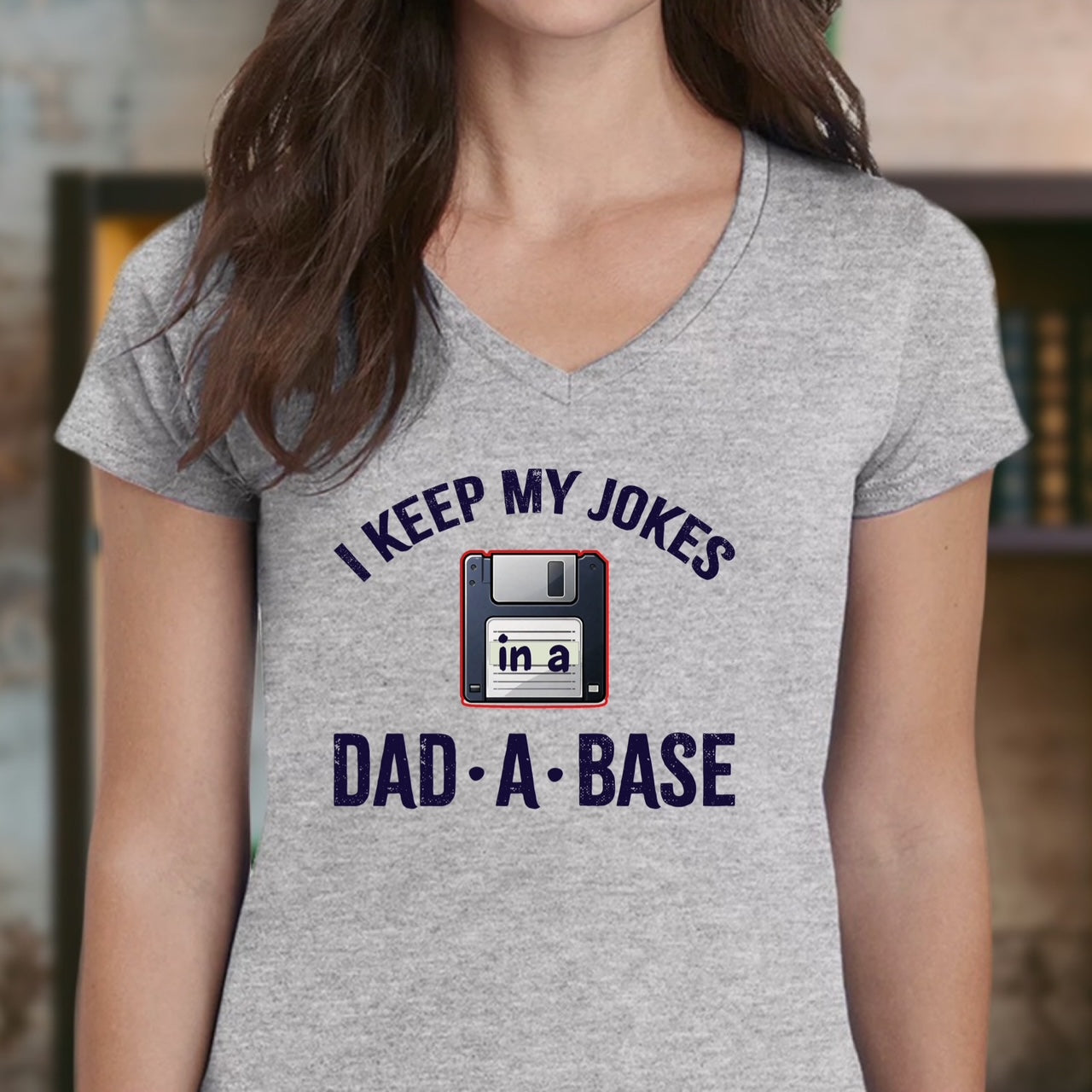 Woman wearing grey v-neck dad joke t-shirt with floppy disk and text I keep my jokes in a dad-a-base