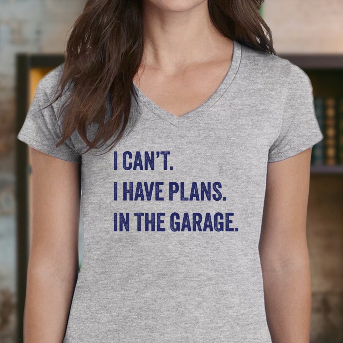 Woman wearing v-neck grey t-shirt with navy lettering I can’t I have plans in the garage
