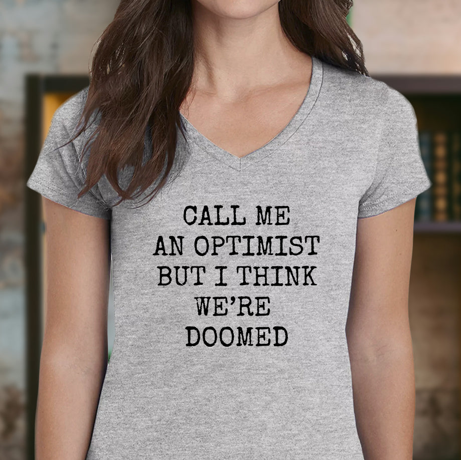 Woman in grey v-neck t-shirt with black text call me an optimist but I think we’re doomed