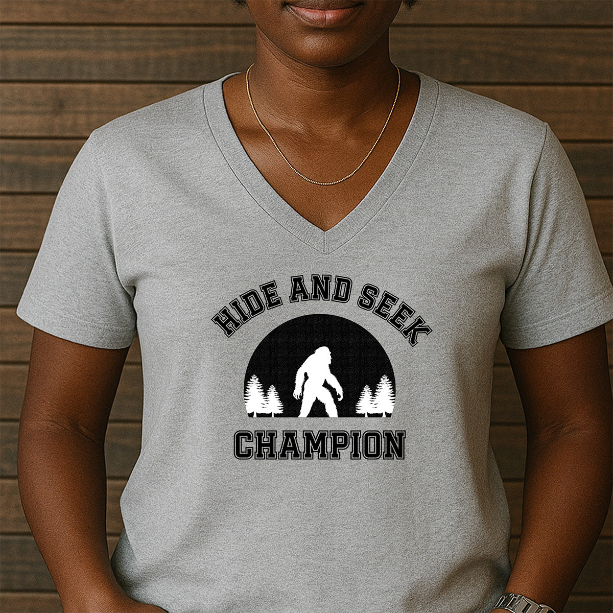 Grey women’s v-neck t-shirt with Hide and Seek Champion slogan and Bigfoot silhouette in trees design